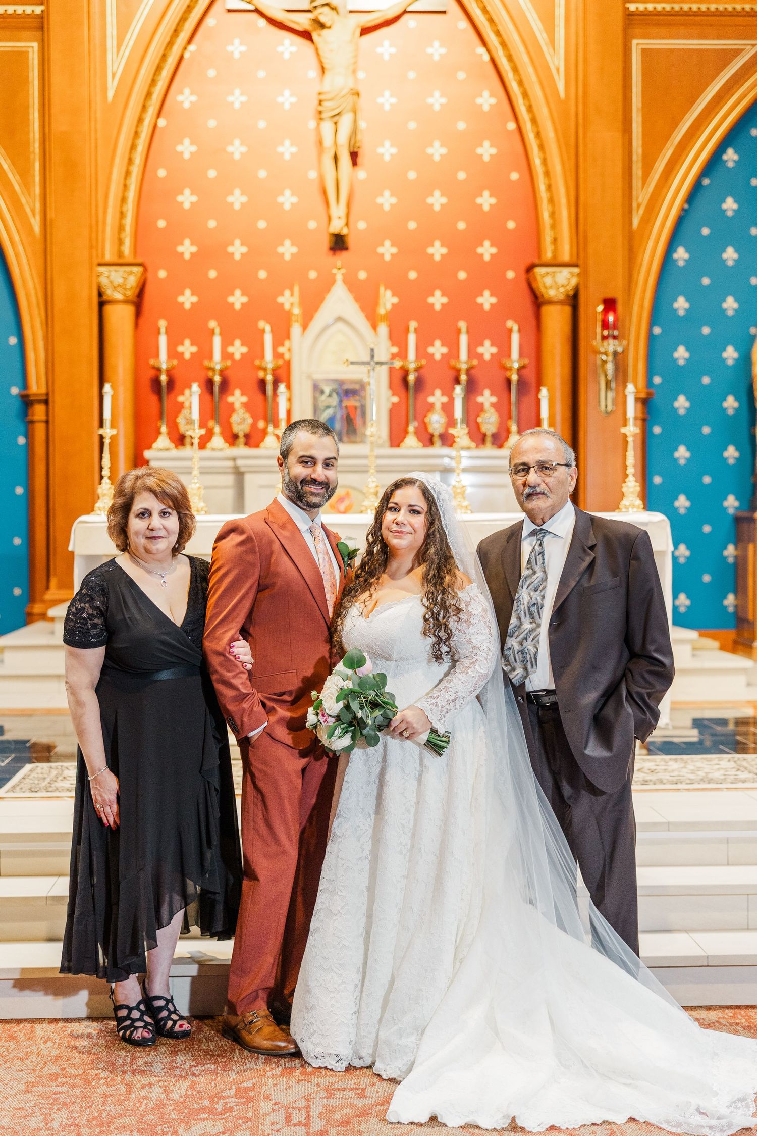 Wedding party poses together in ornate church with colorful stained glass windows and decorative arches.