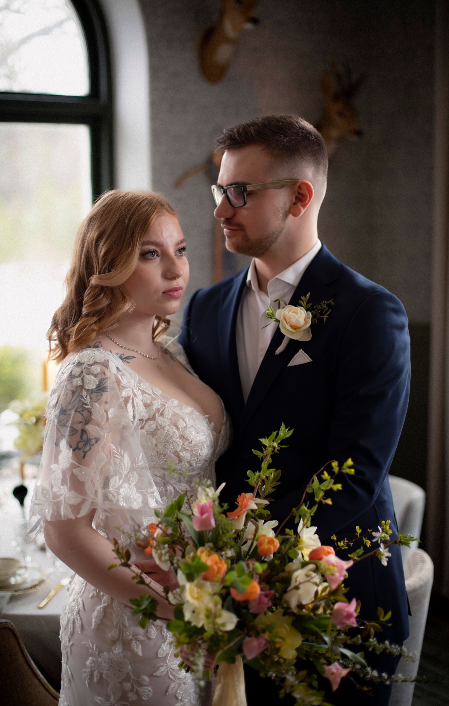 bröllopsfotografering inomhus. bruden håller i en bukett och brudgummen håller om bruden. mannen  har en blå kostym med en gul ros i fickan.