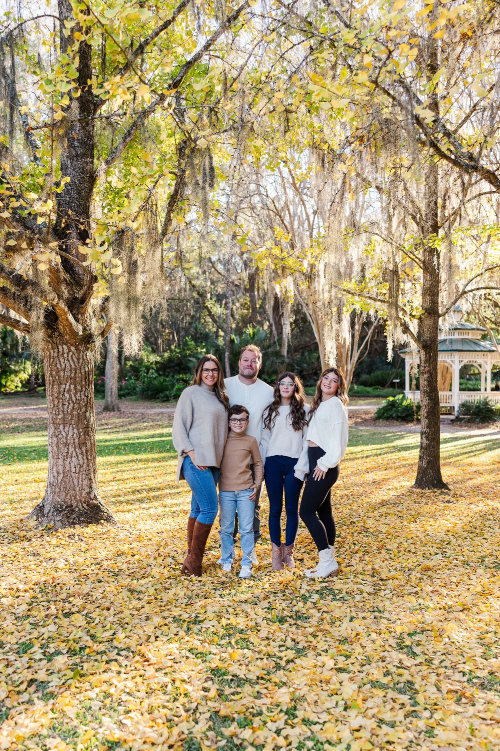 Group stands together on fallen autumn leaves beneath Spanish moss draped trees in a scenic park setting.