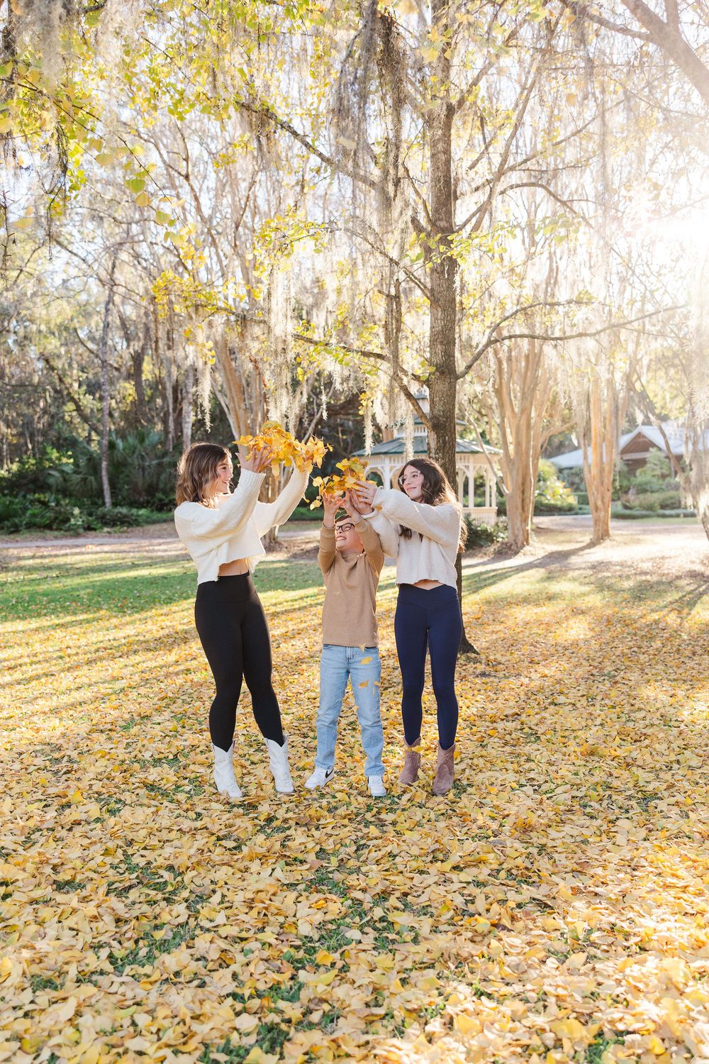 A playful group poses and jumps among golden fall leaves in a wooded park setting.