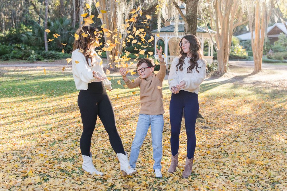 A group walking together through a park during autumn with fallen yellow leaves scattered on the ground.