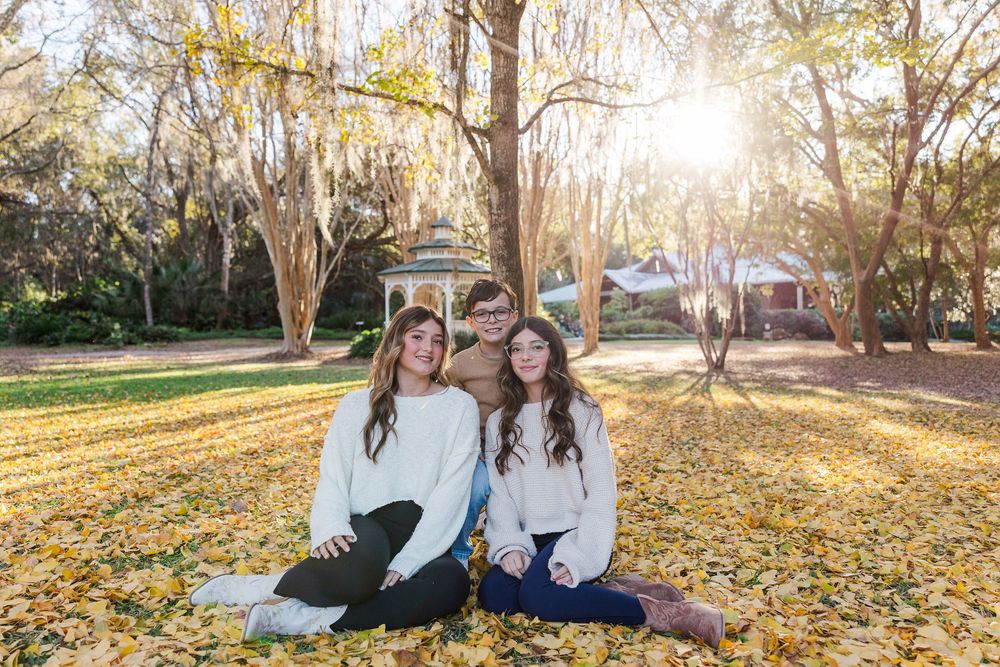 A family enjoys a golden autumn afternoon together in a park with fallen leaves during sunset.