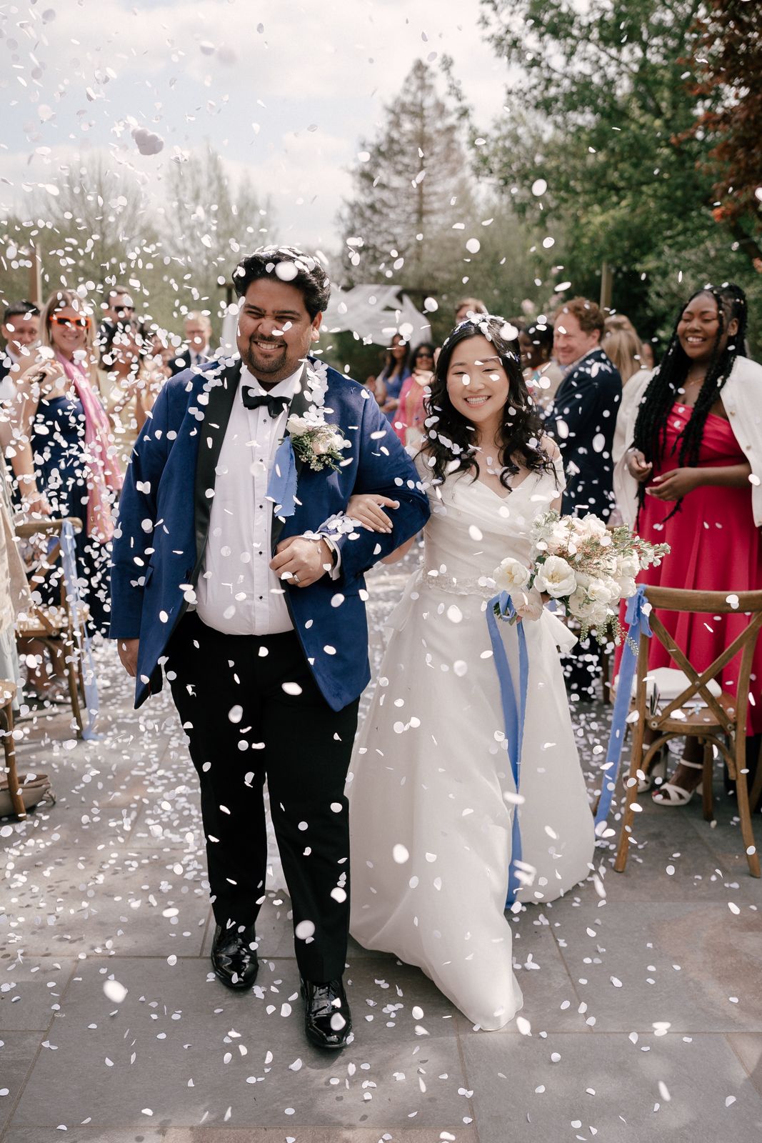 A joyful wedding couple walks down the aisle while guests shower them with white confetti on their special day.