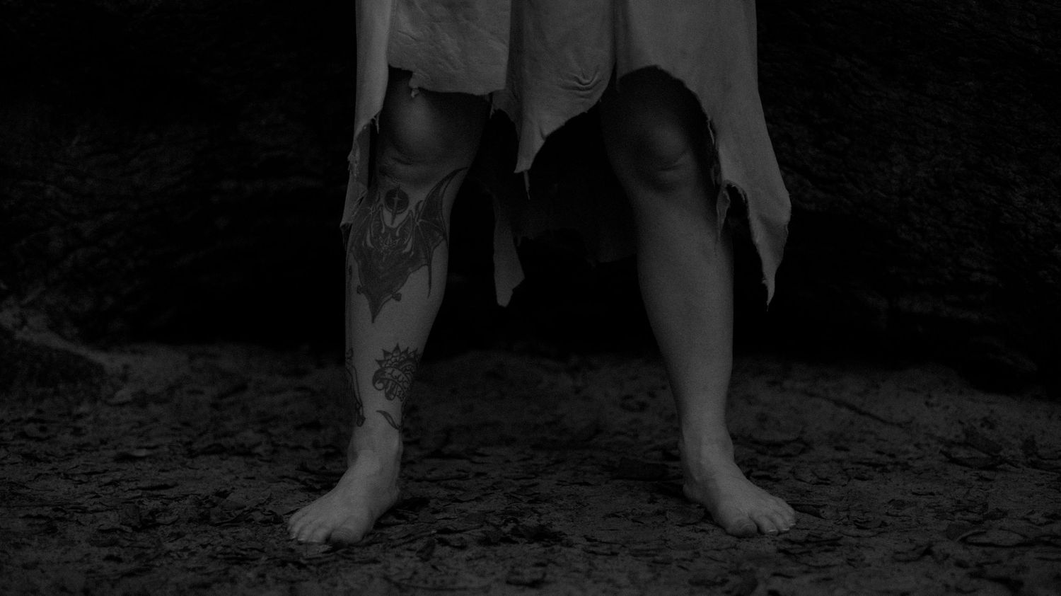 A black and white photograph shows feet walking across a sandy beach at night.