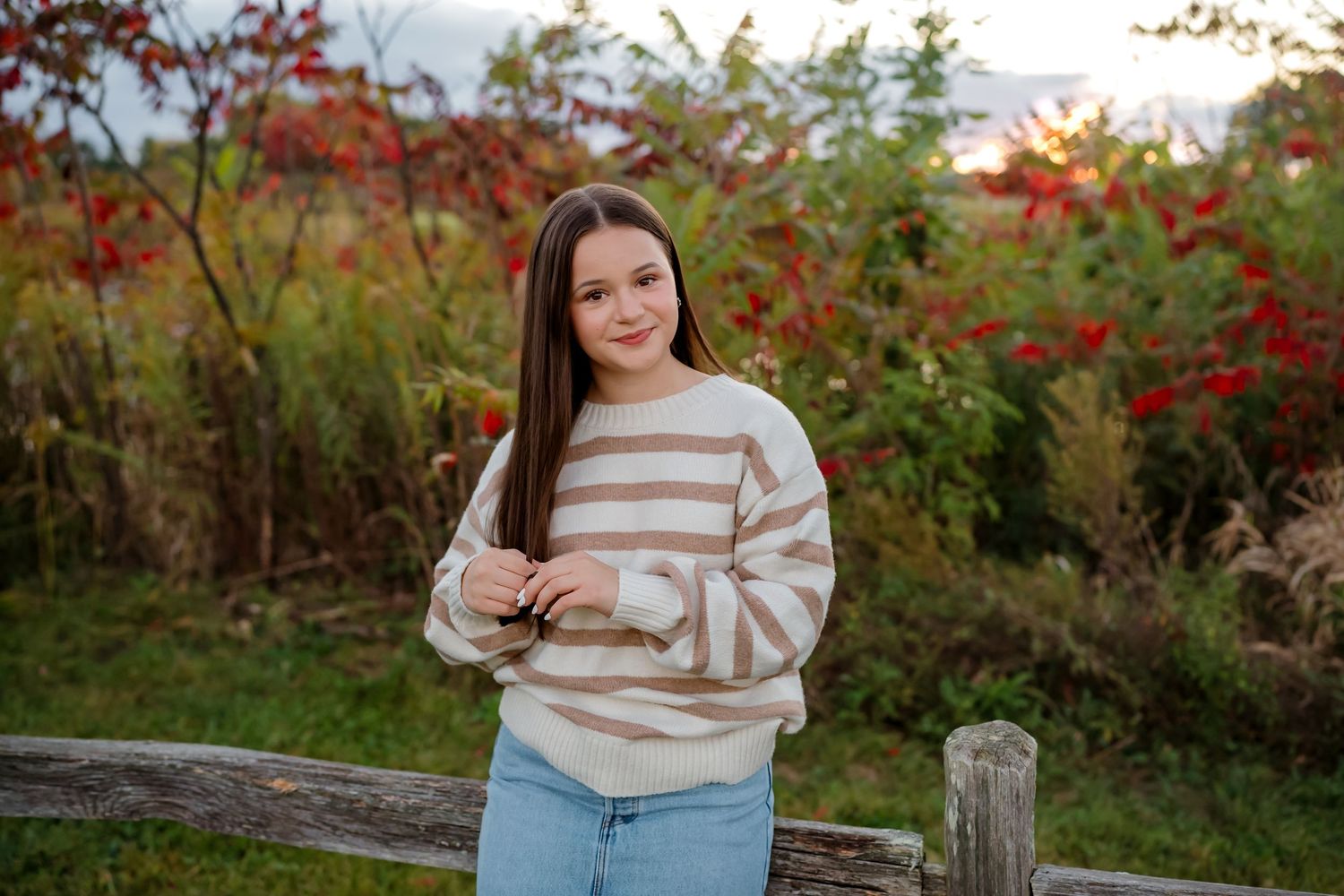 A fall photography session in a field with red foliage and natural golden sunlight creating a warm autumn atmosphere.