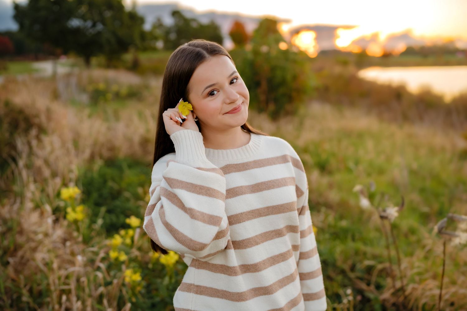 Person in striped sweater poses in golden sunlit meadow during sunset photo session.