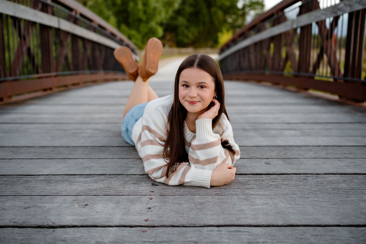 Young woman in white sweater lying on wooden bridge deck during outdoor photo session.