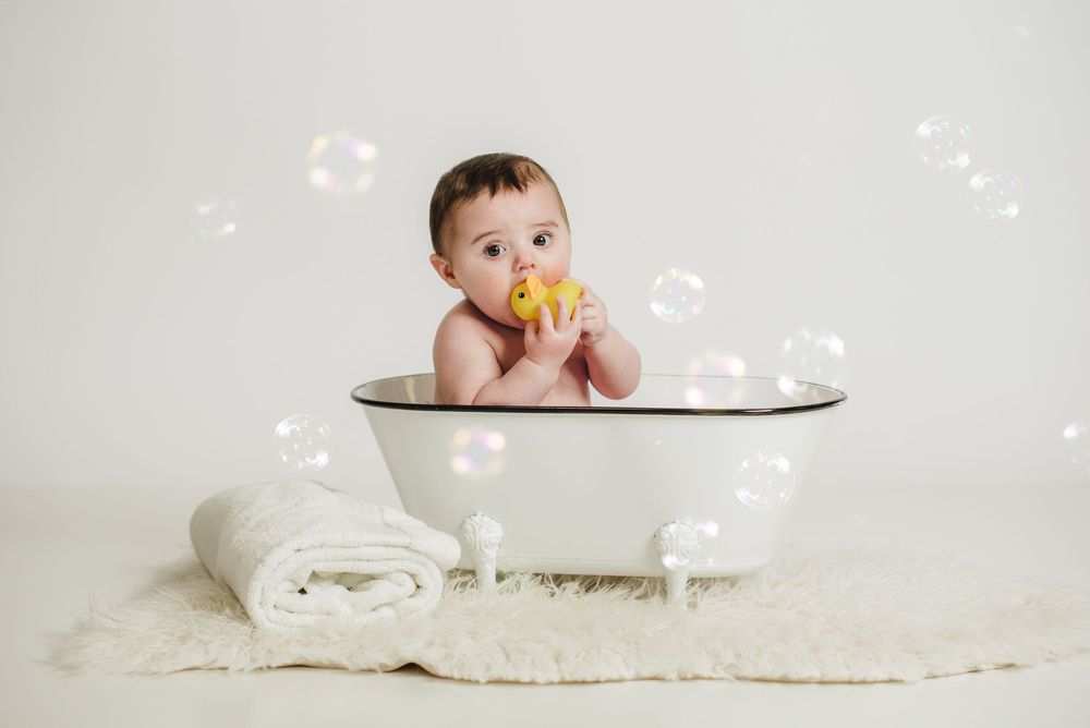 Baby lying on white blanket surrounded by floating soap bubbles.