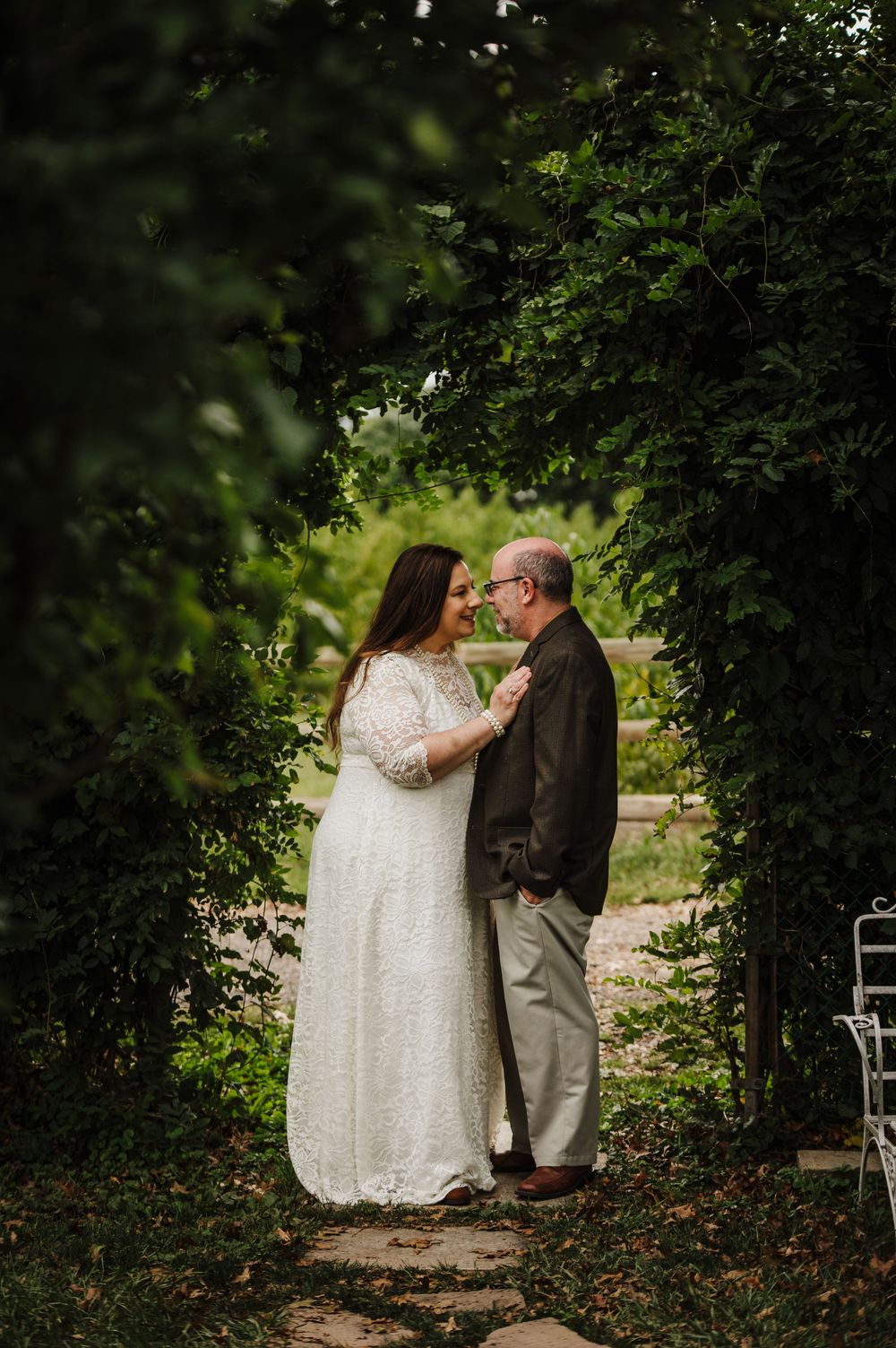 Couple sharing intimate moment on garden path surrounded by greenery.