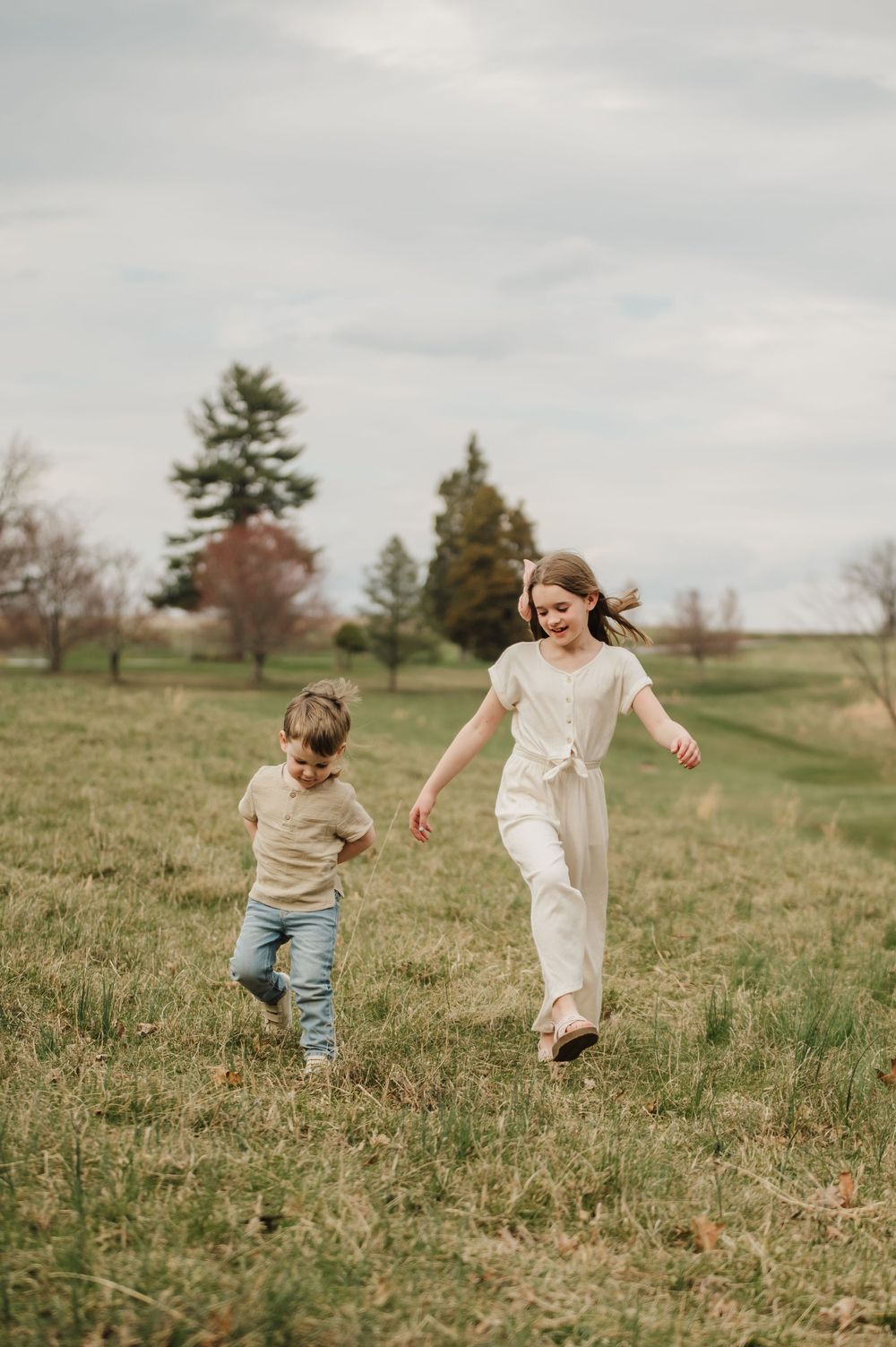 Children run and play together in a grassy field on a cloudy day.