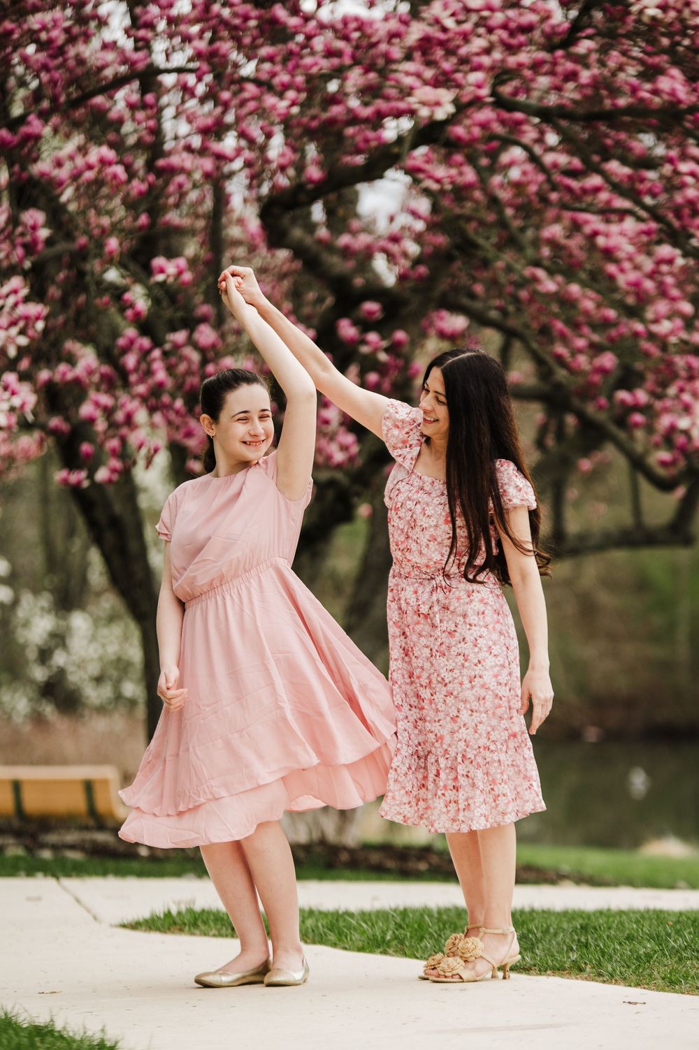Two children in pink dresses twirl under blooming cherry blossom trees.