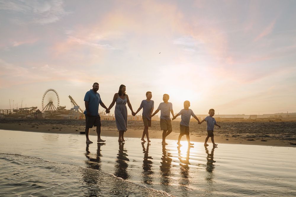 Silhouettes of people holding hands in ocean water during sunset.