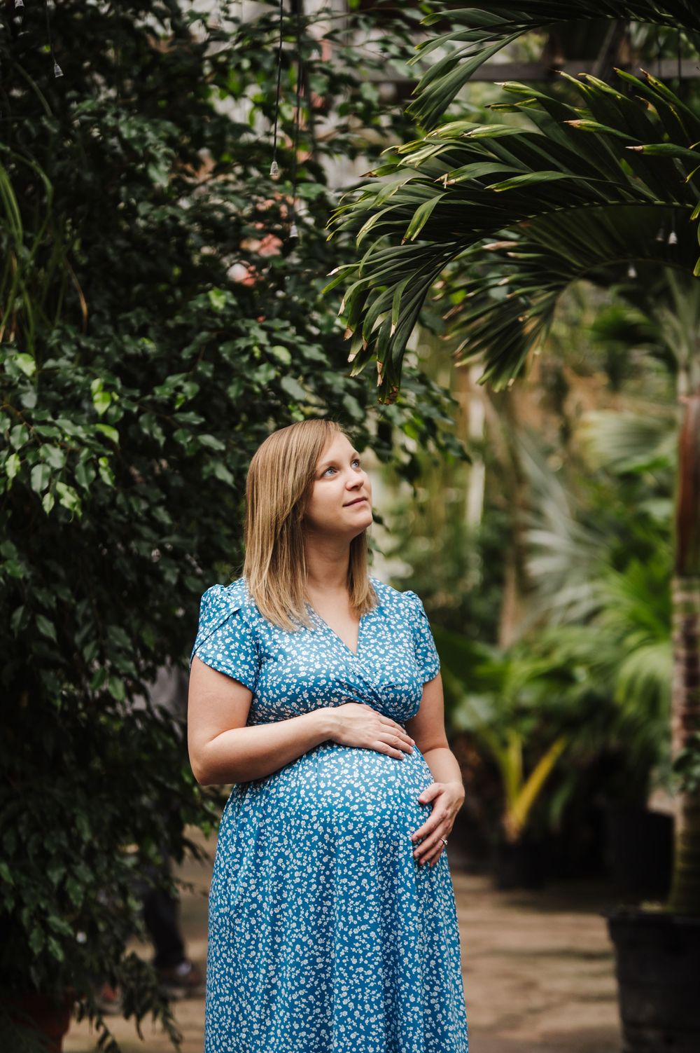 Woman in blue polka dot dress standing in lush garden setting.