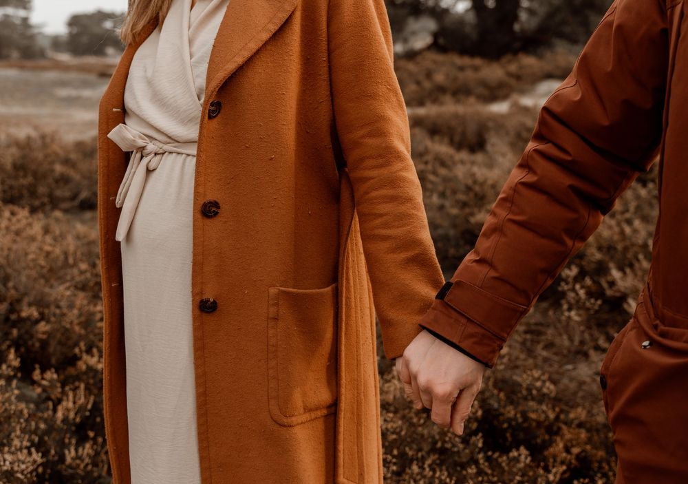 A person wearing a brown coat stands in an outdoor field during golden hour lighting.
