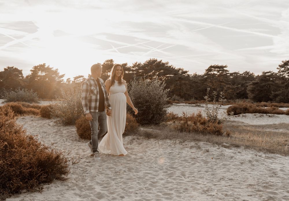 Couple strolling together on a sandy beach path surrounded by coastal vegetation at golden hour.