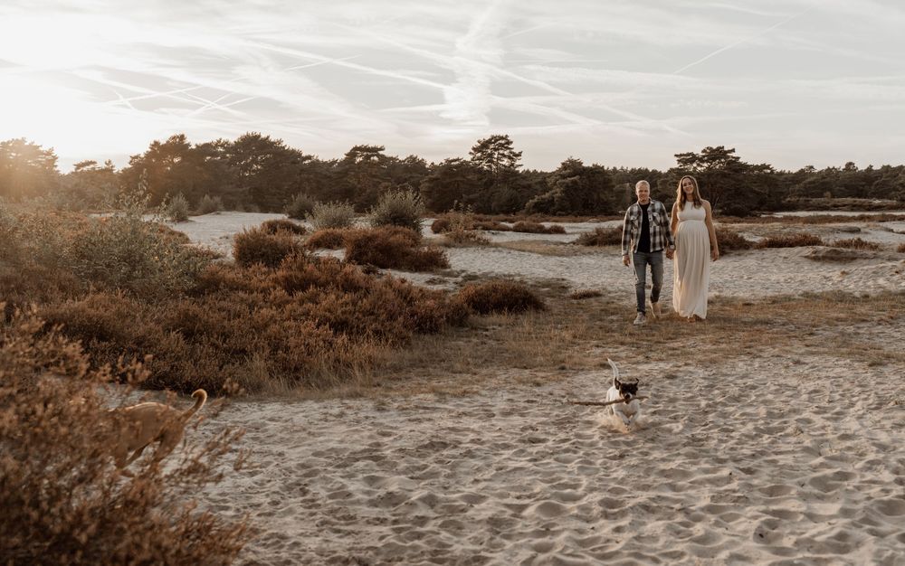 A couple walks along a sandy beach path through coastal vegetation at sunset in sepia tones.
