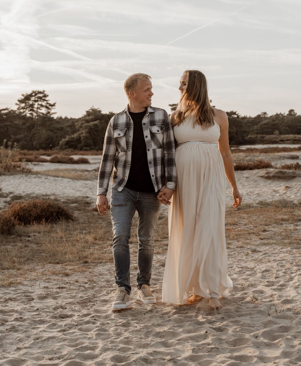 A couple walks hand in hand on a sandy beach during sunset in matching cream and plaid outfits.