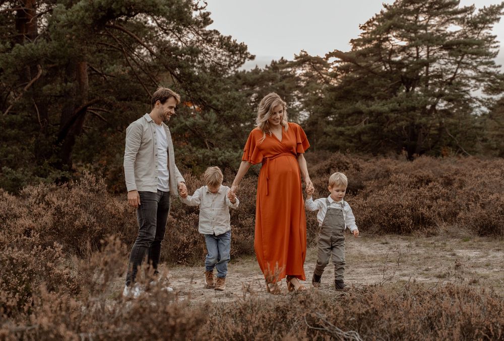 A family walks together on a forest path during sunset, with pine trees and autumn foliage in the background.