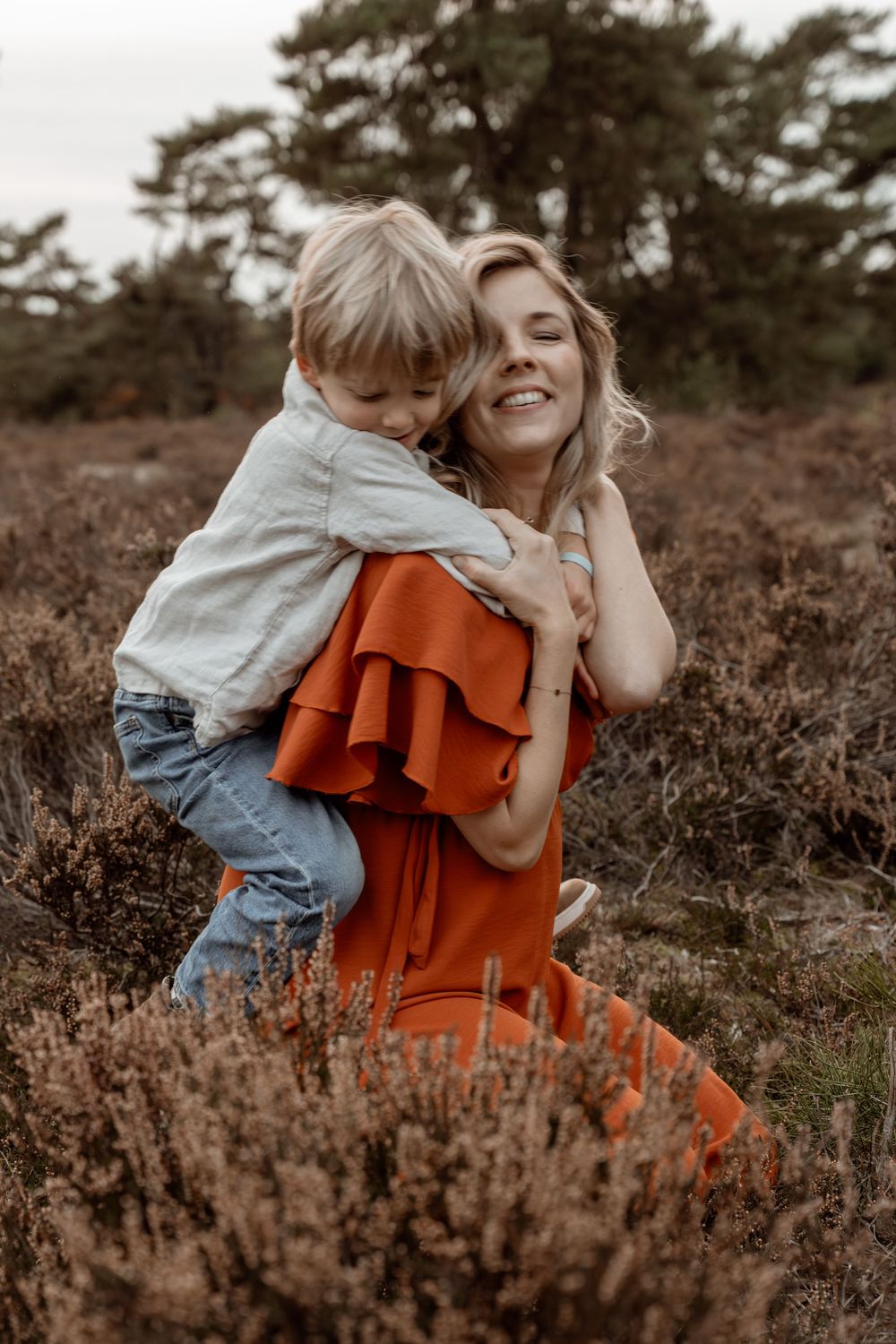 Two figures in a field of heather, one wearing a rust-colored dress and the other in light denim, share a tender moment.