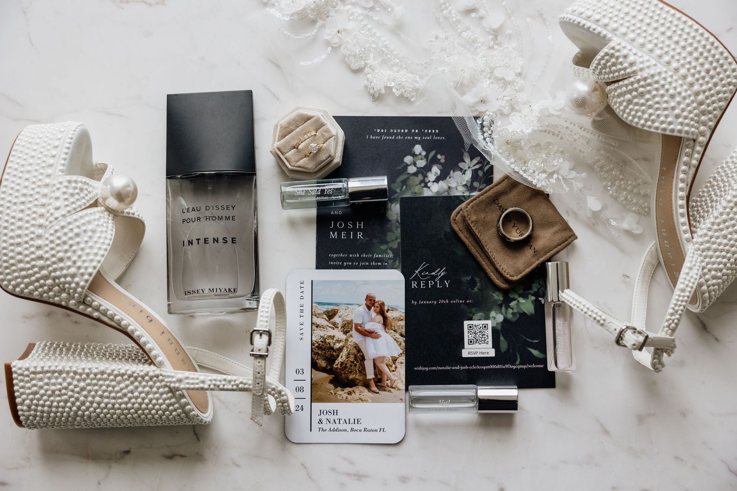 Fragrance bottle and black packaging arranged with white knit boots and fashion accessories on marble surface.