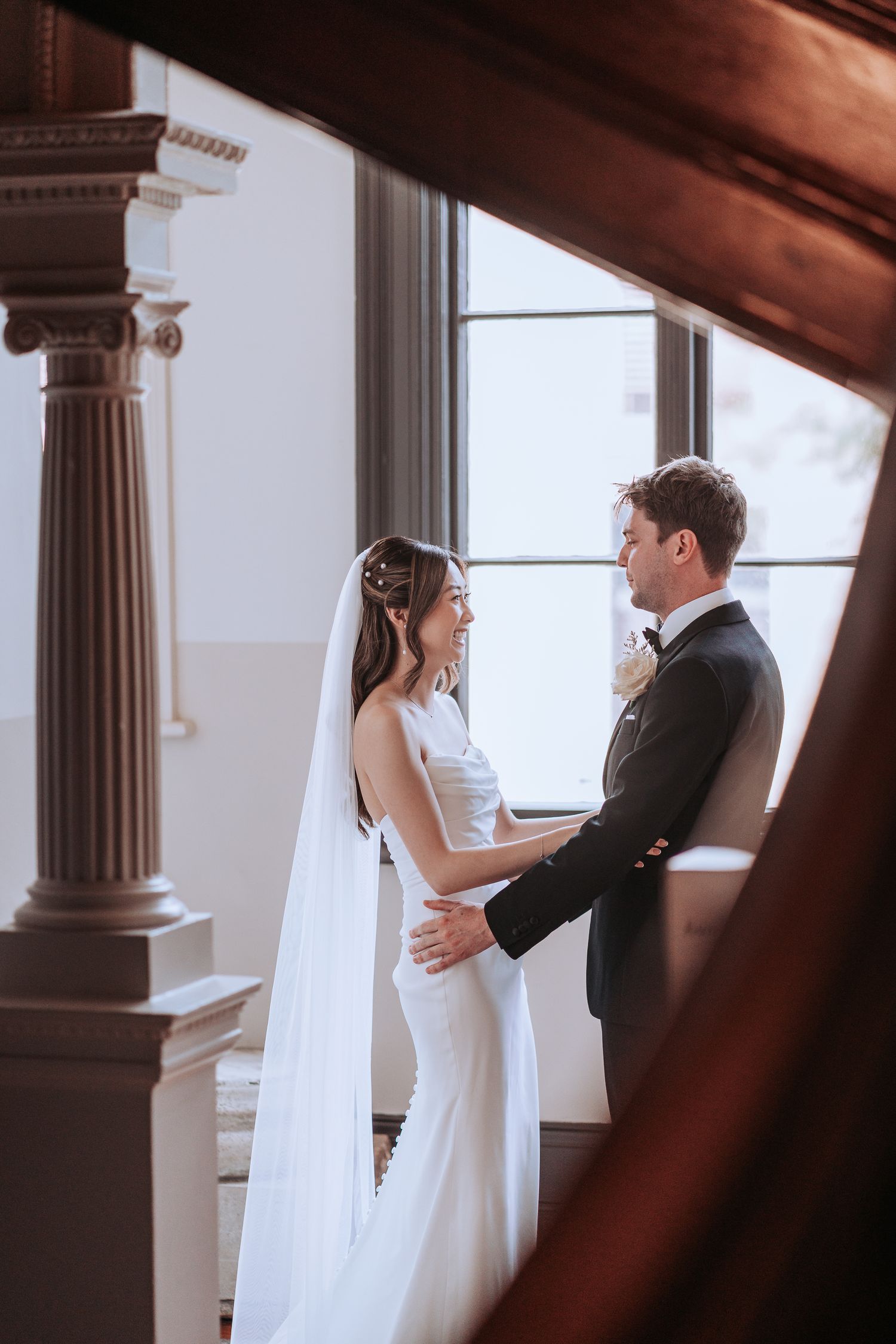 A romantic wedding moment captured between columns with natural window lighting.