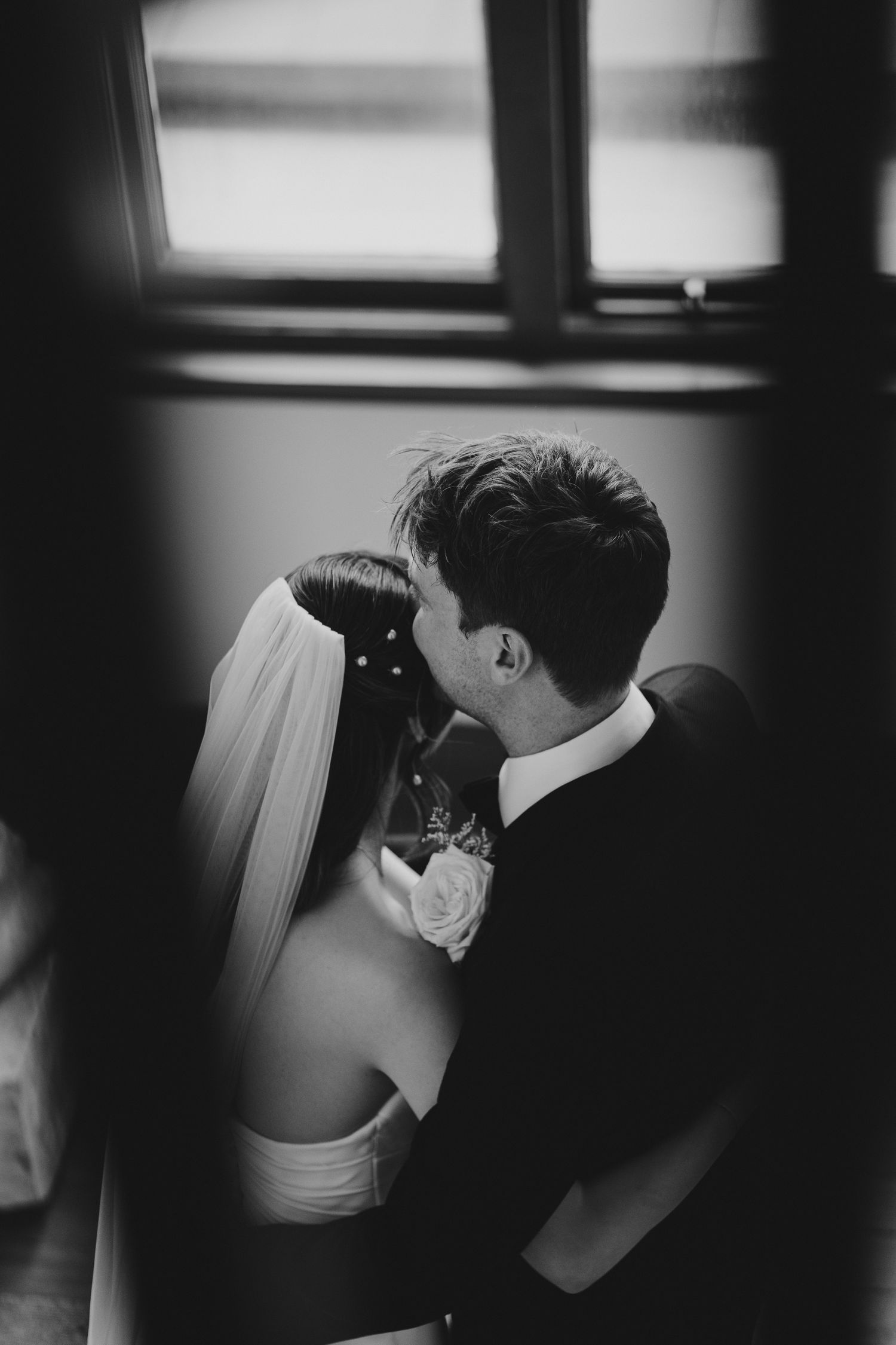 A tender black and white wedding moment captured through window light.