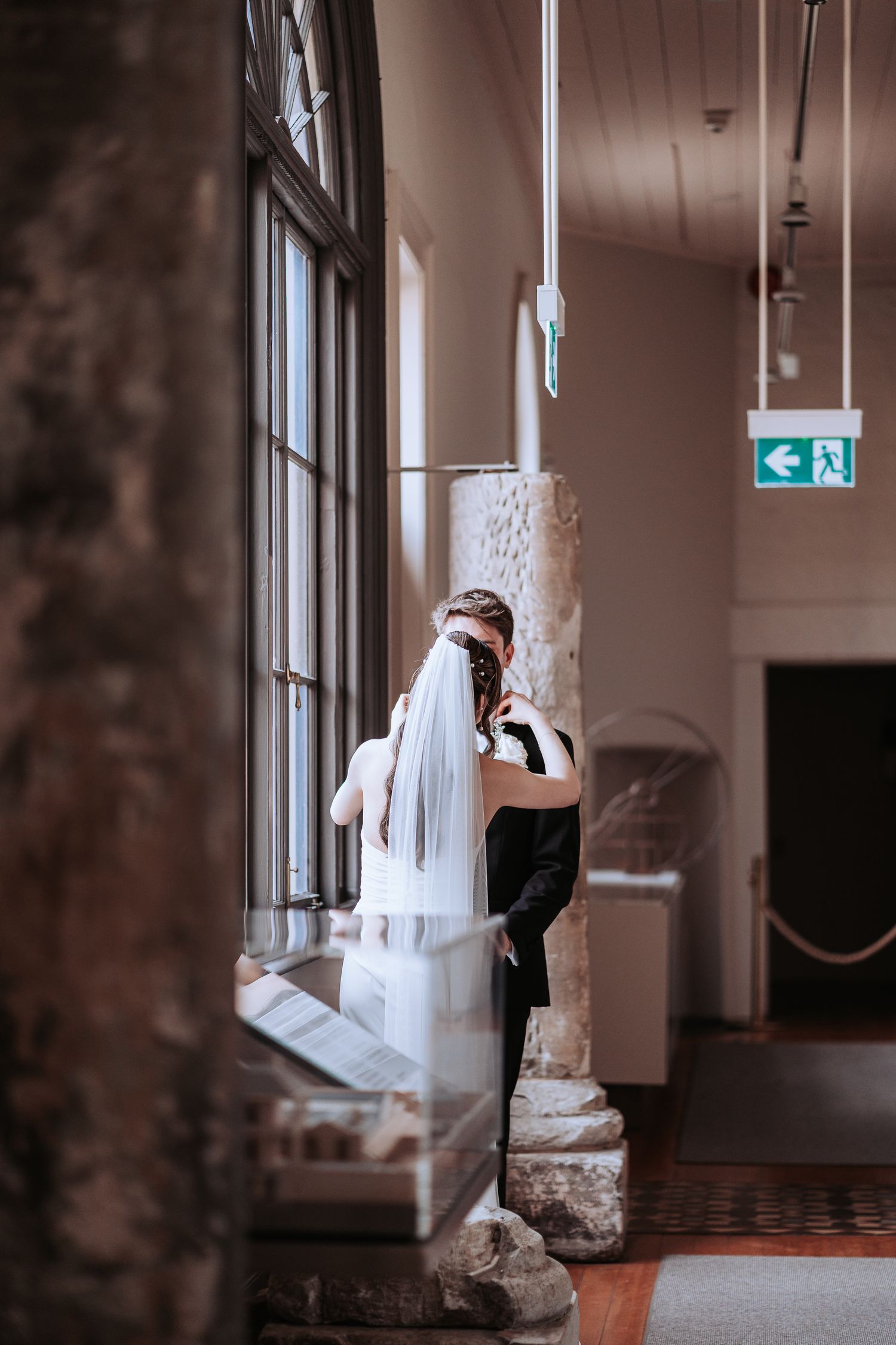 A wedding couple shares an intimate moment by classical columns and windows.