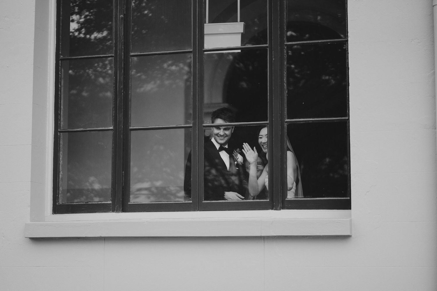 Black and white photo of couple posing through window during wedding photoshoot.
