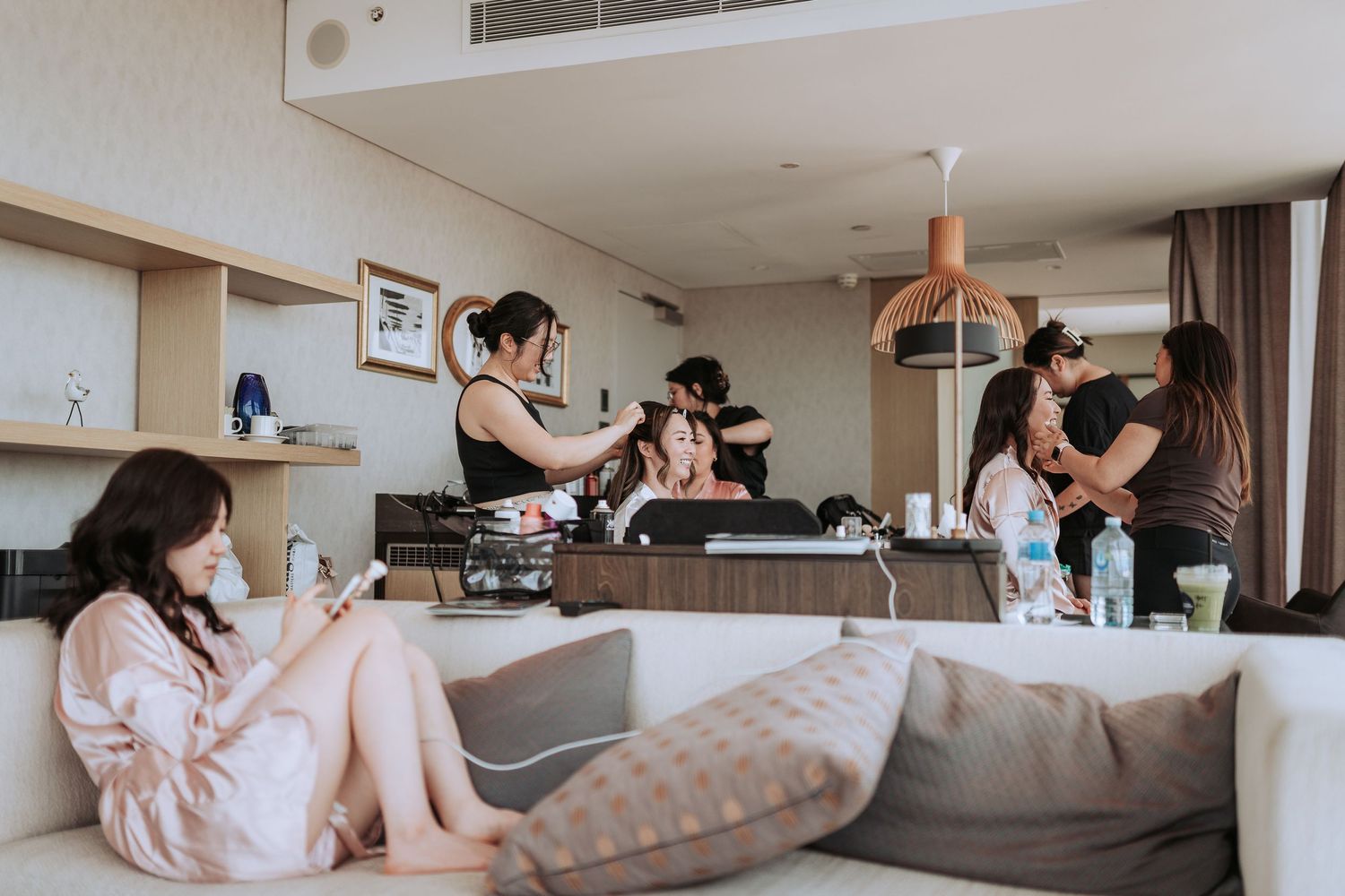 Wedding preparation scene with multiple stylists working in a modern hotel room.