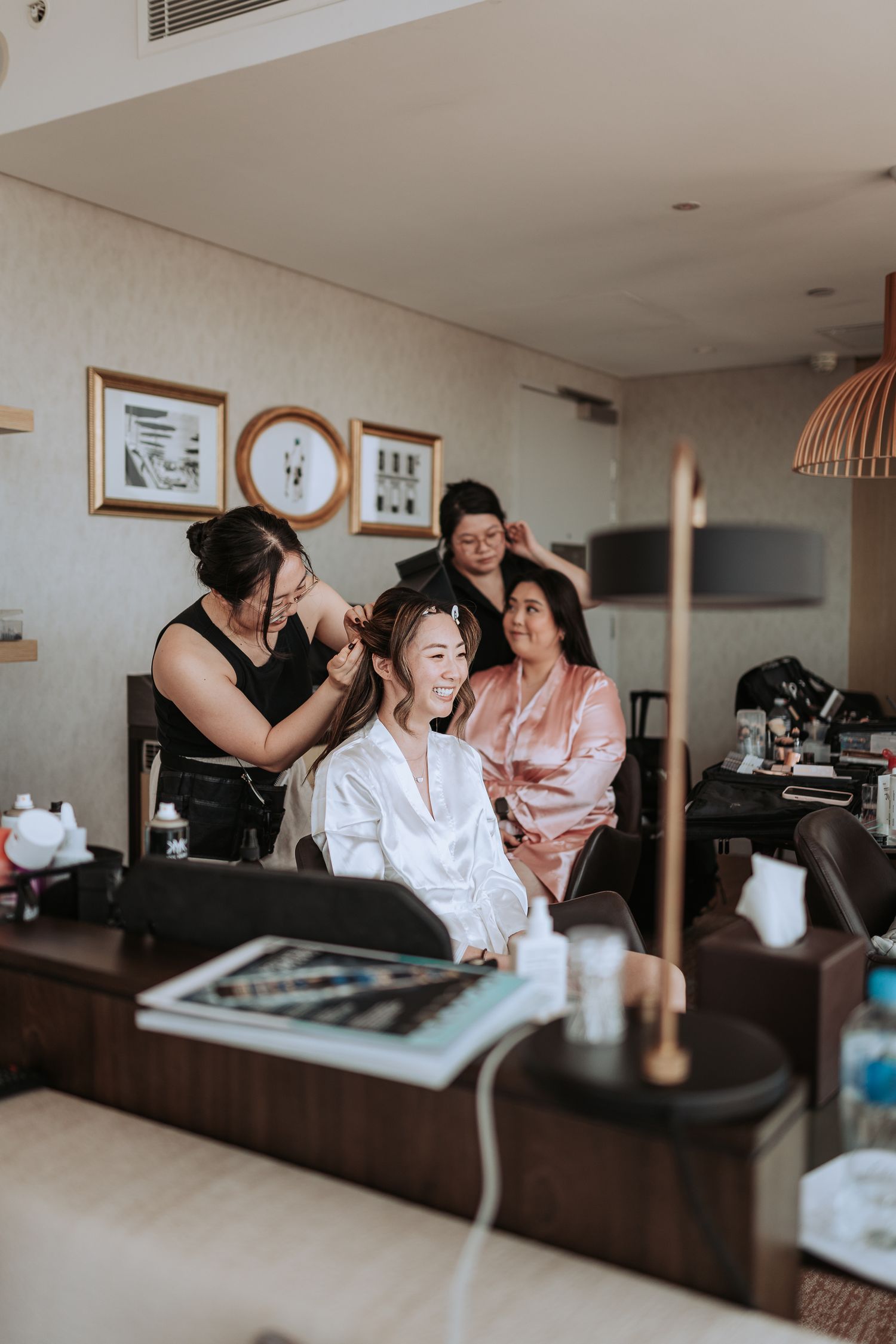 Bridal preparation scene with stylists working on hair and makeup in a modern setting.