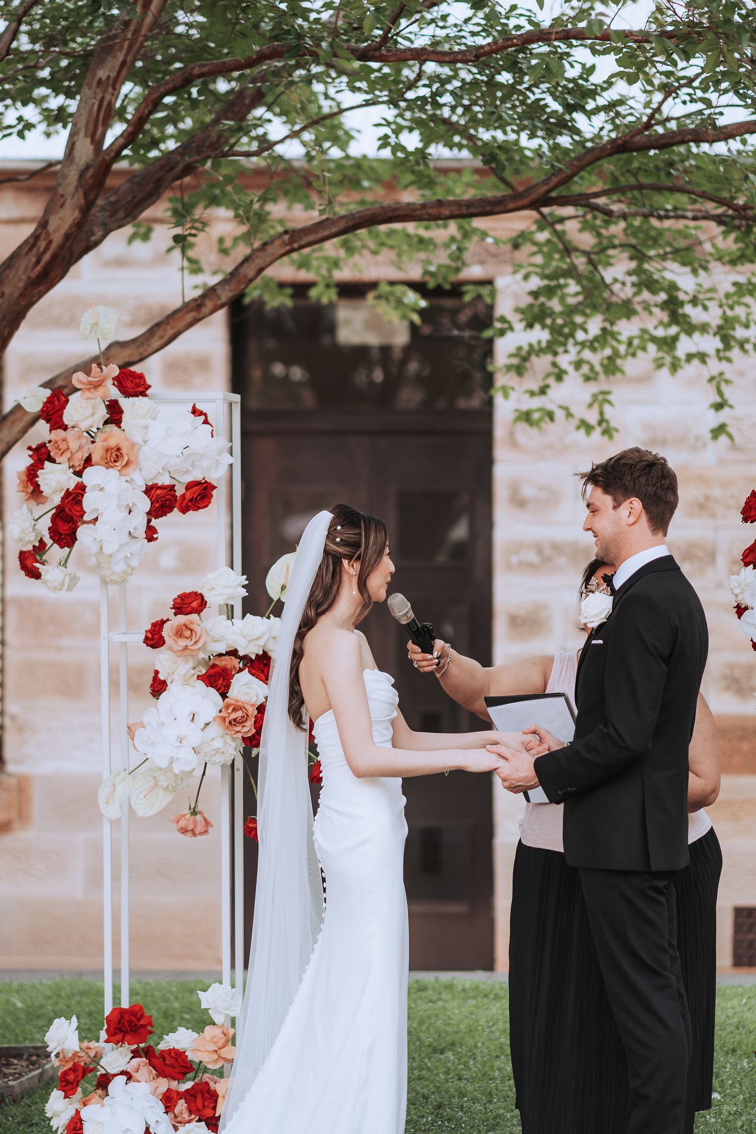Couple exchanging vows during outdoor wedding ceremony decorated with red and white flowers.