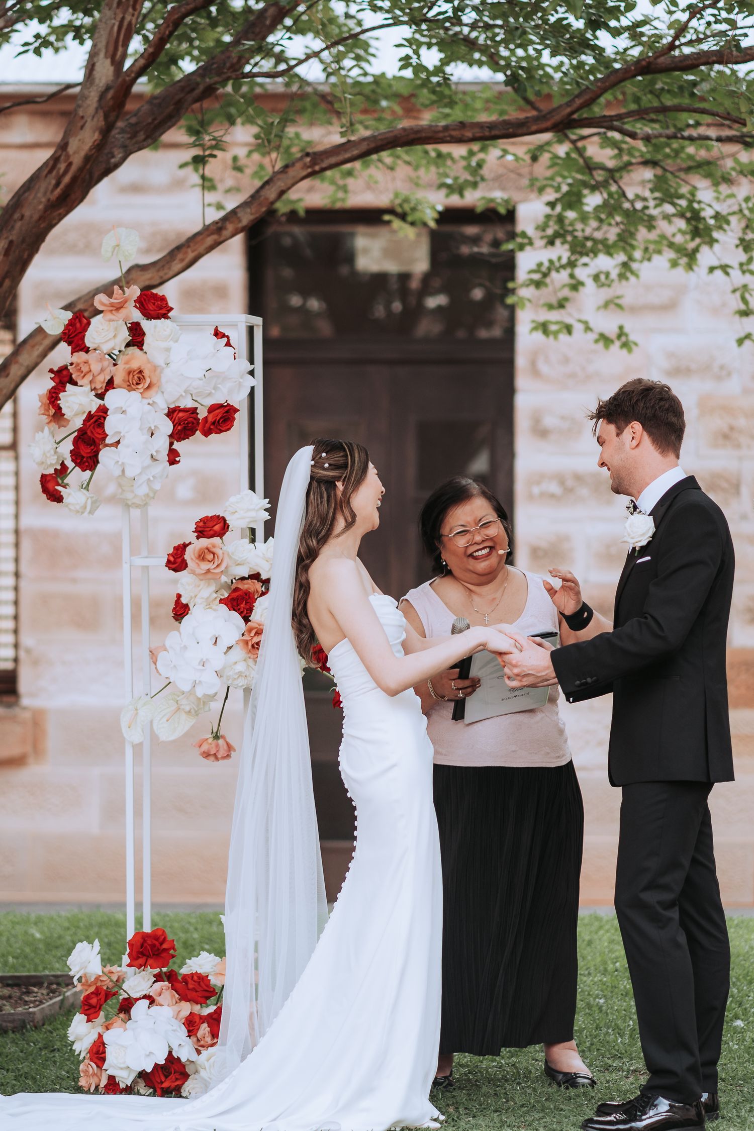 Wedding ceremony moment with officiant and couple under tree with floral decorations.