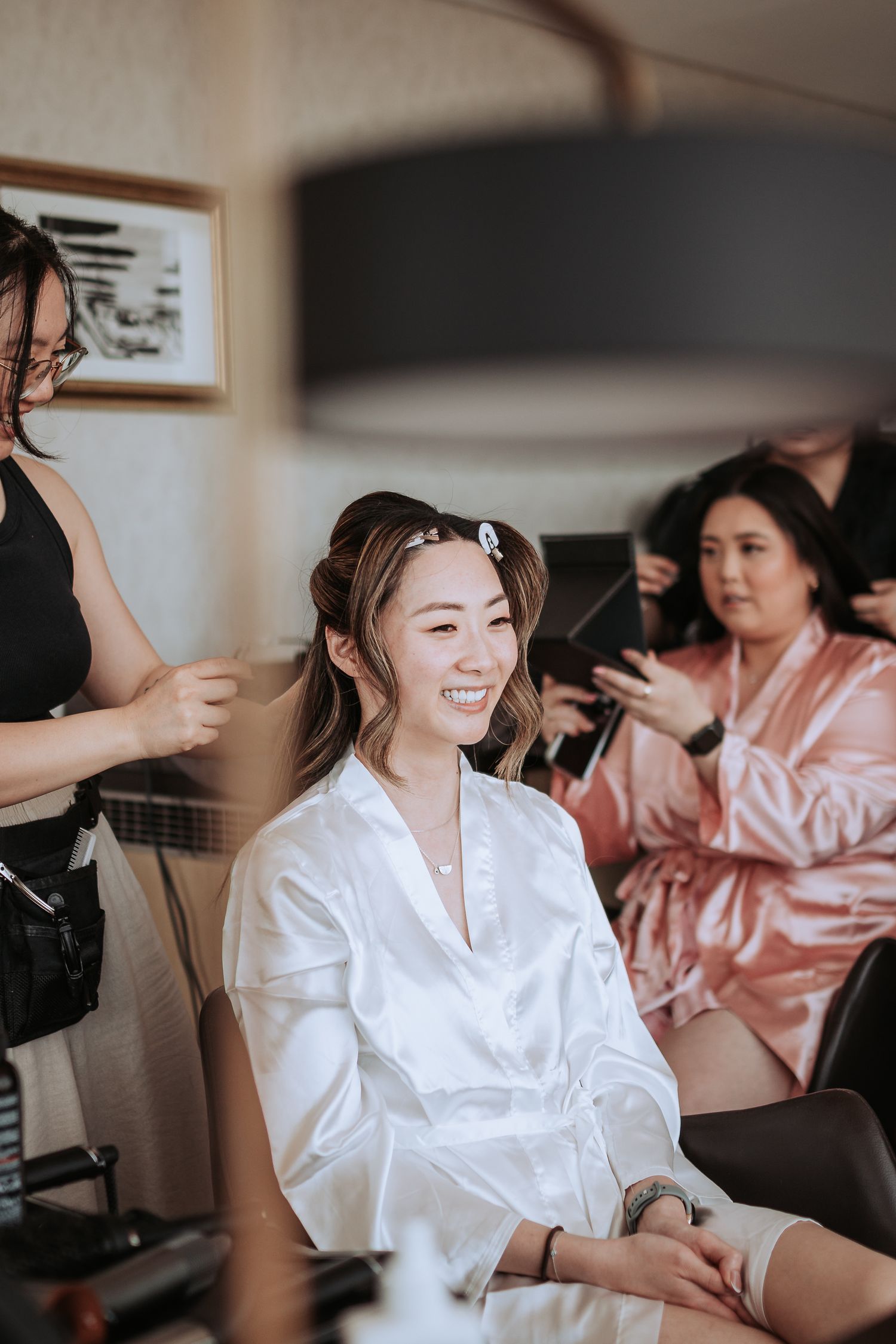 Joyful preparation moment with hair and makeup stylists working in a bright room.
