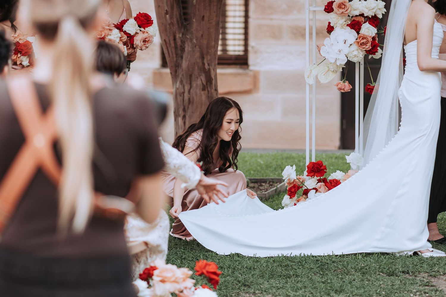 Wedding dress train being arranged during outdoor ceremony with floral decorations.