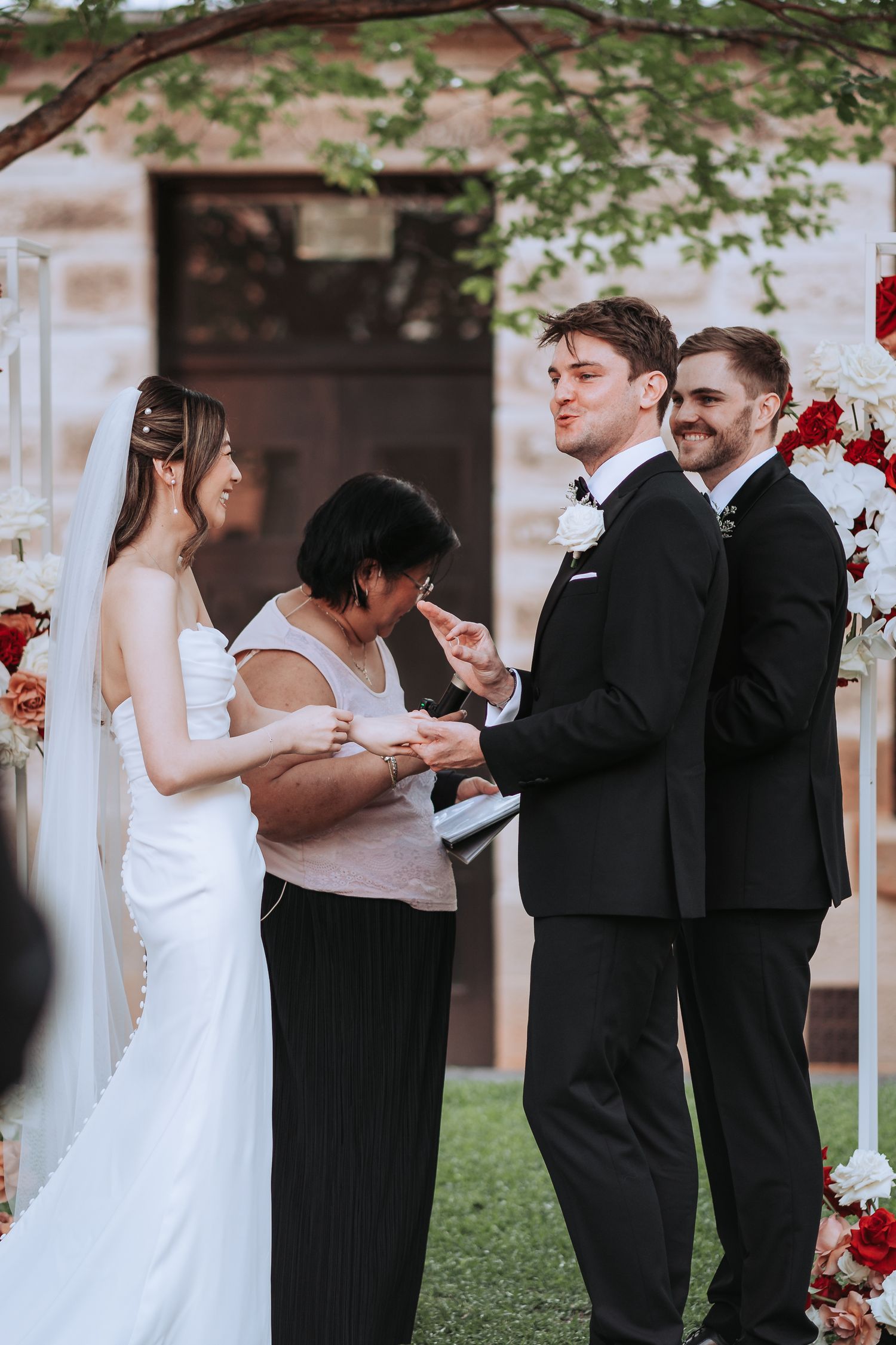 Wedding party gathered during ceremony with red and white floral decorations.
