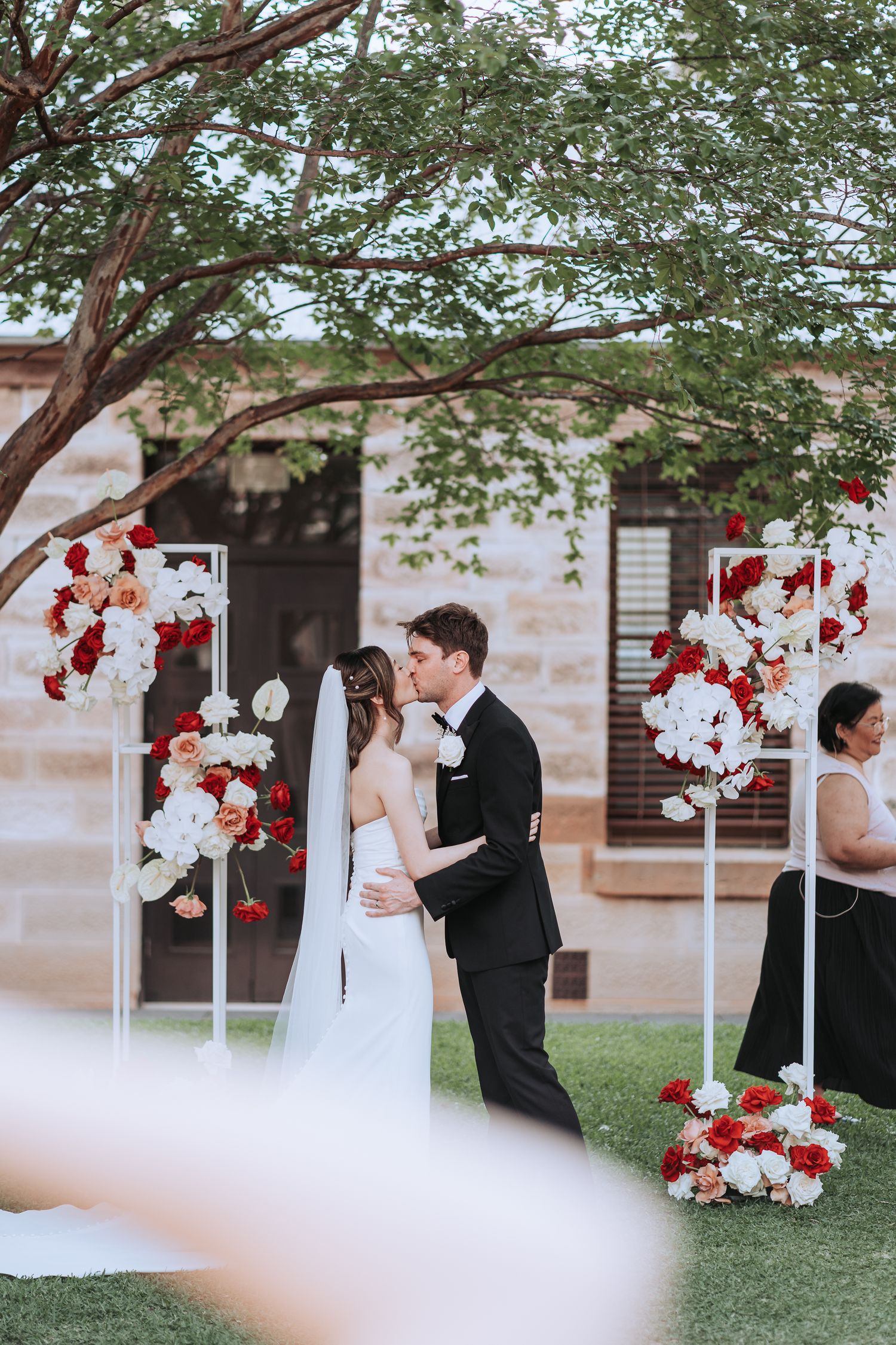 Intimate moment during outdoor wedding ceremony with red and white floral stands.