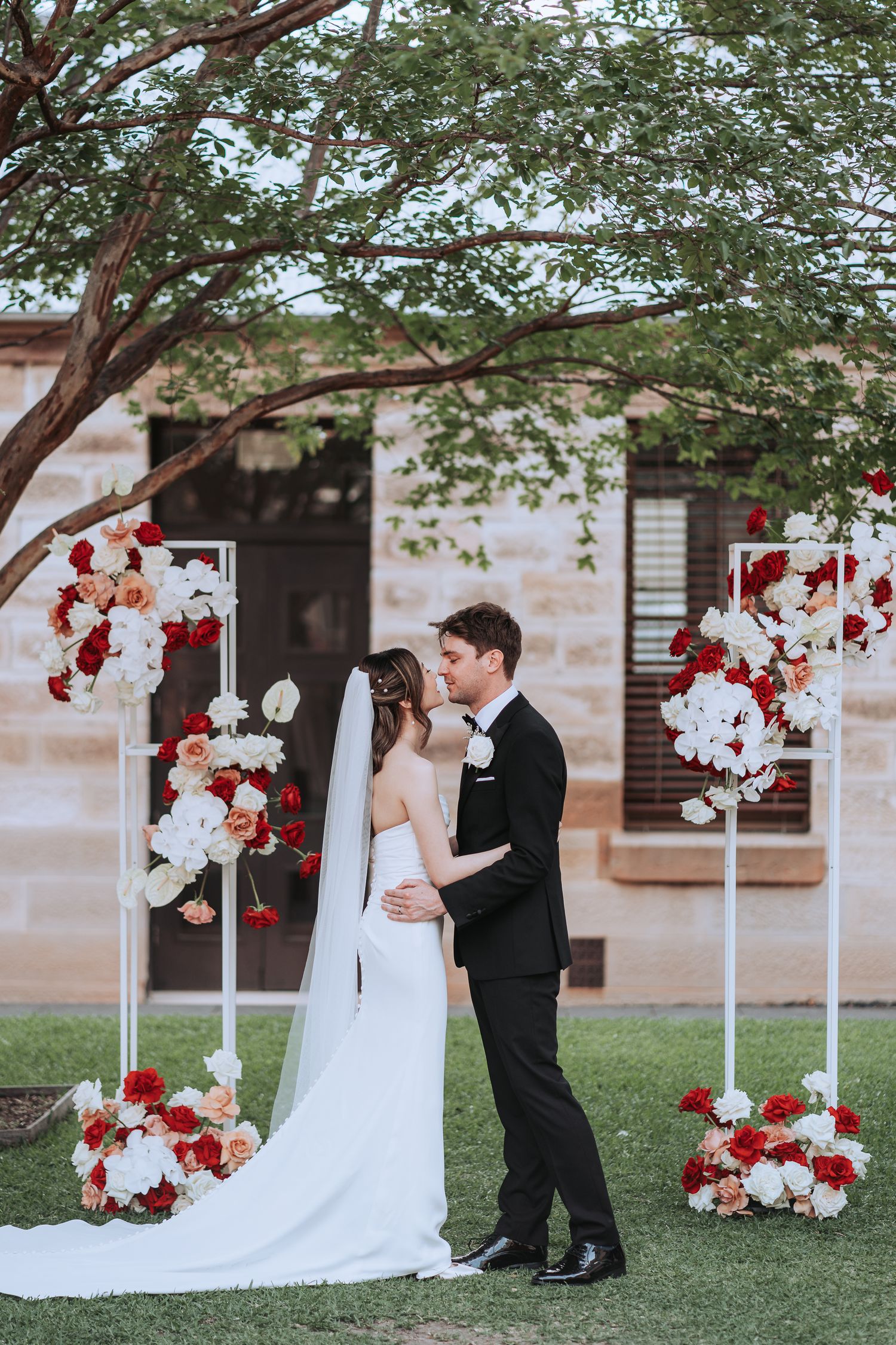 Romantic moment at outdoor wedding with red and white floral decorations on stands.