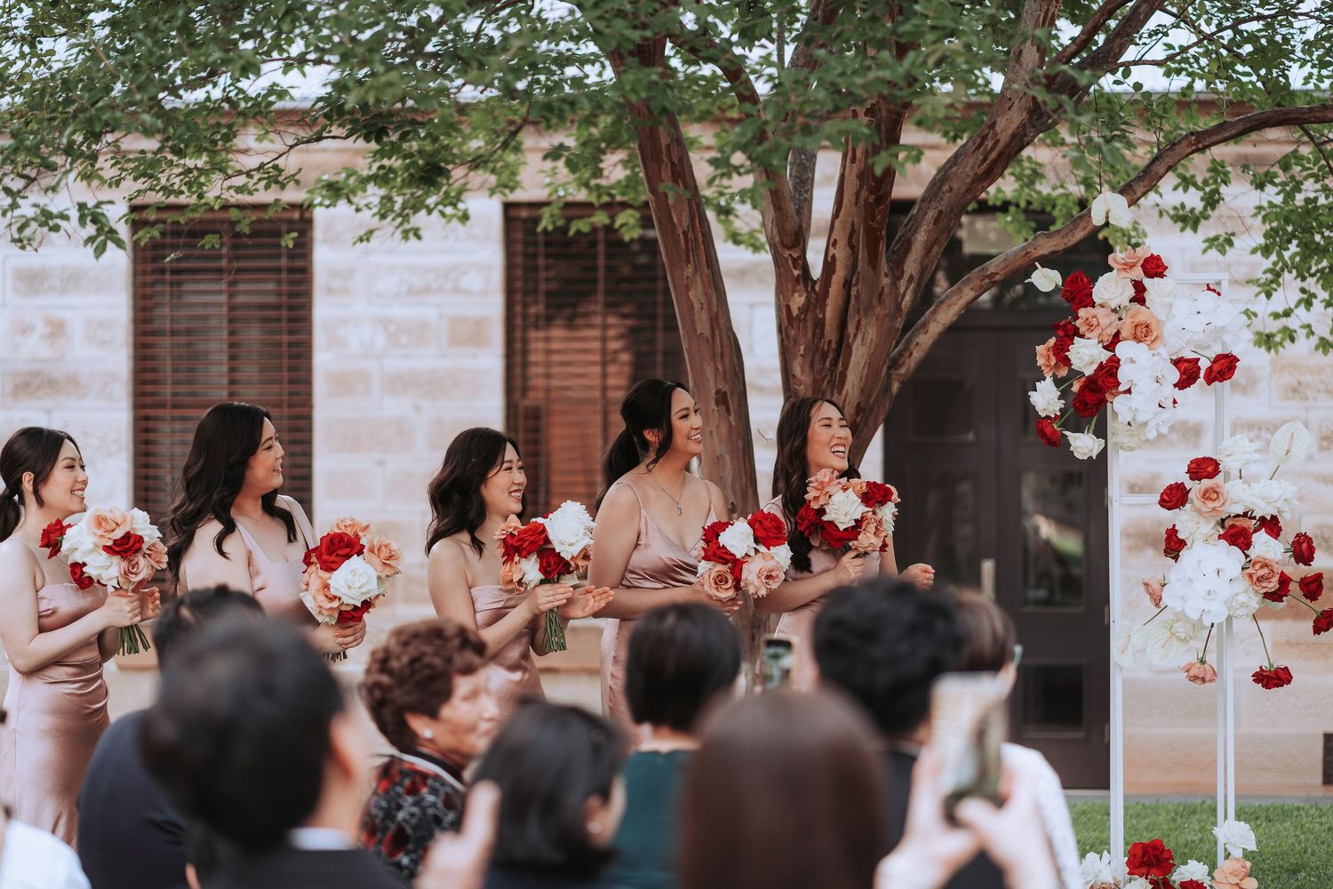 Wedding party in formal attire watching ceremony with red and white floral decorations.
