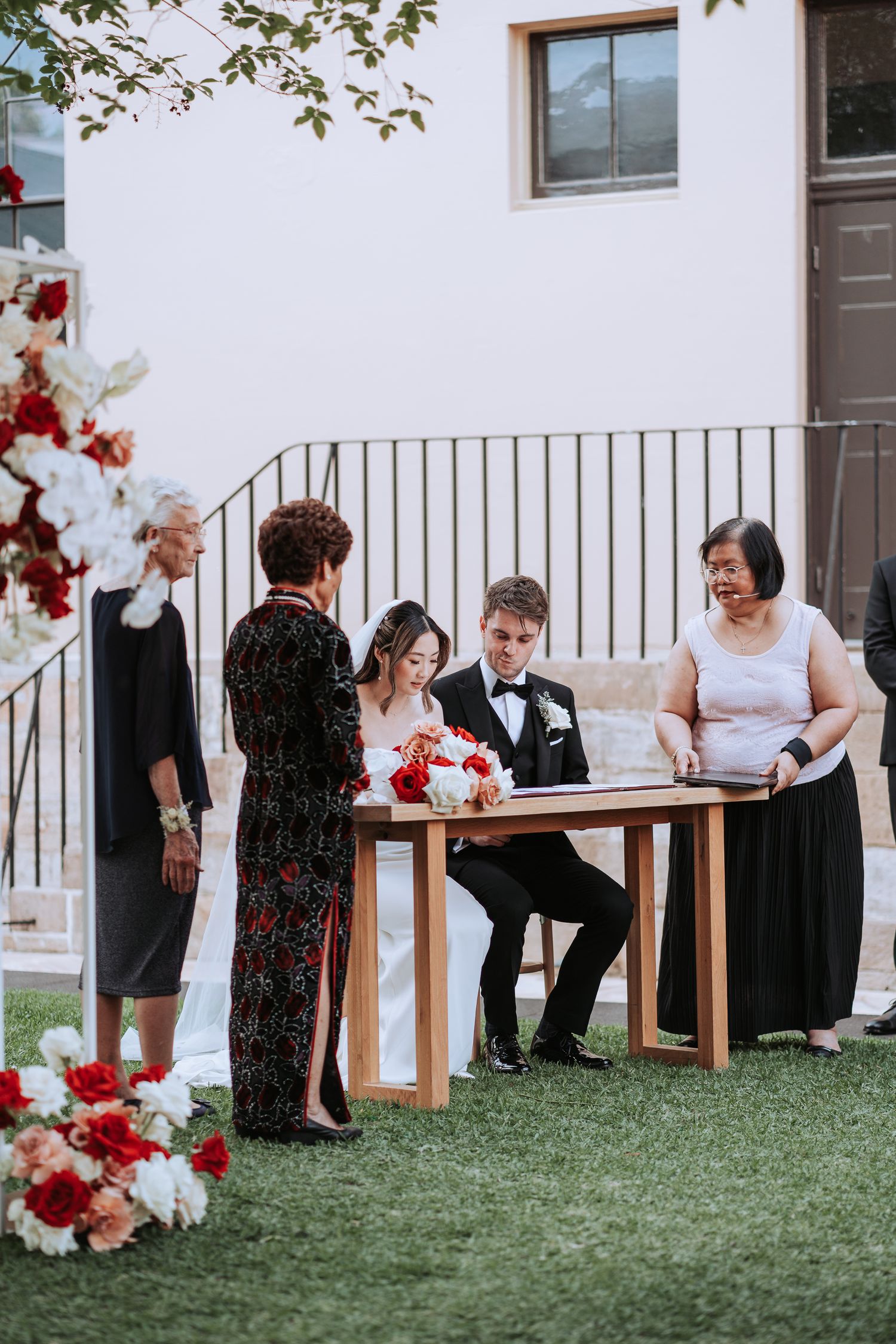 Wedding ceremony signing moment at wooden table with floral decorations on lawn.