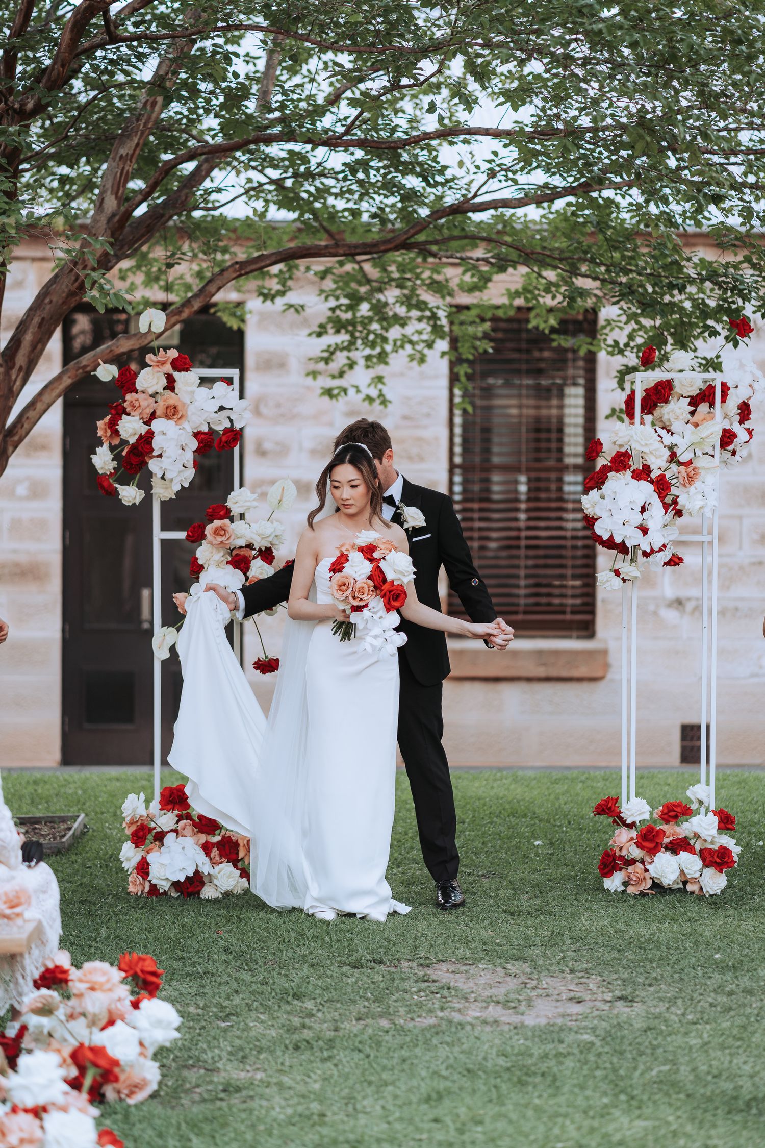Joyful wedding moment captured with red and white floral stands decorating outdoor ceremony space.