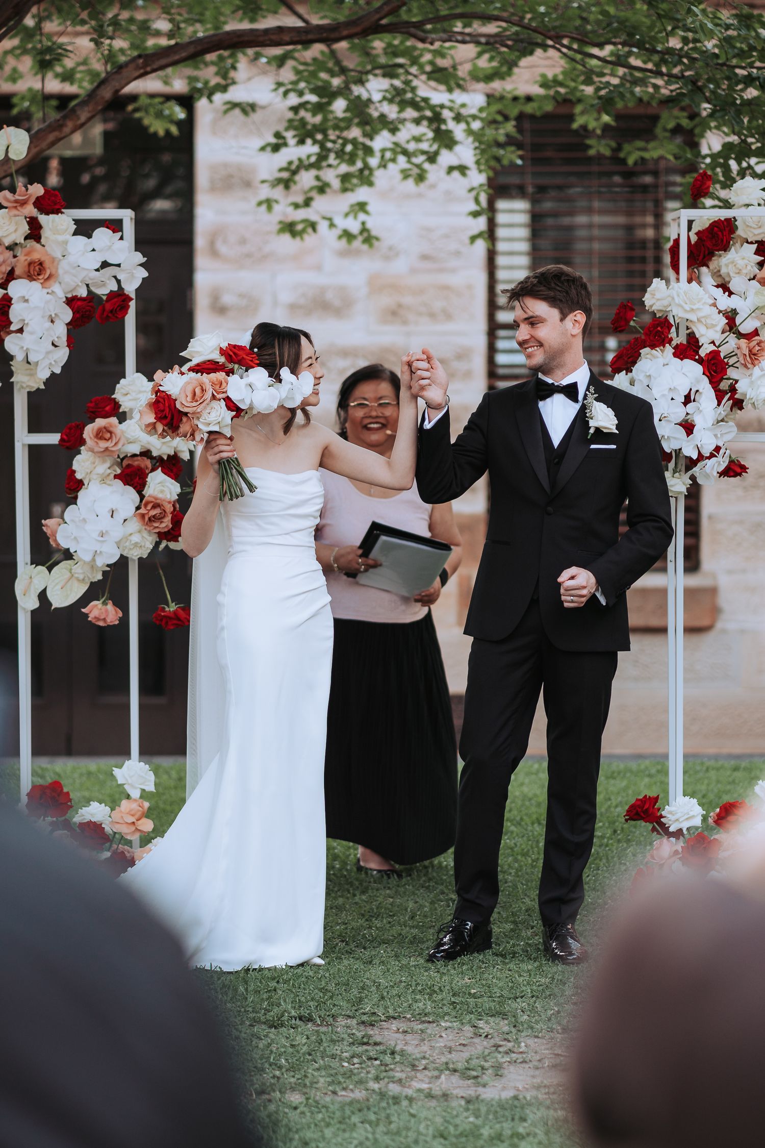 Wedding celebration with red and white floral arch as couple shares joyful moment during ceremony.
