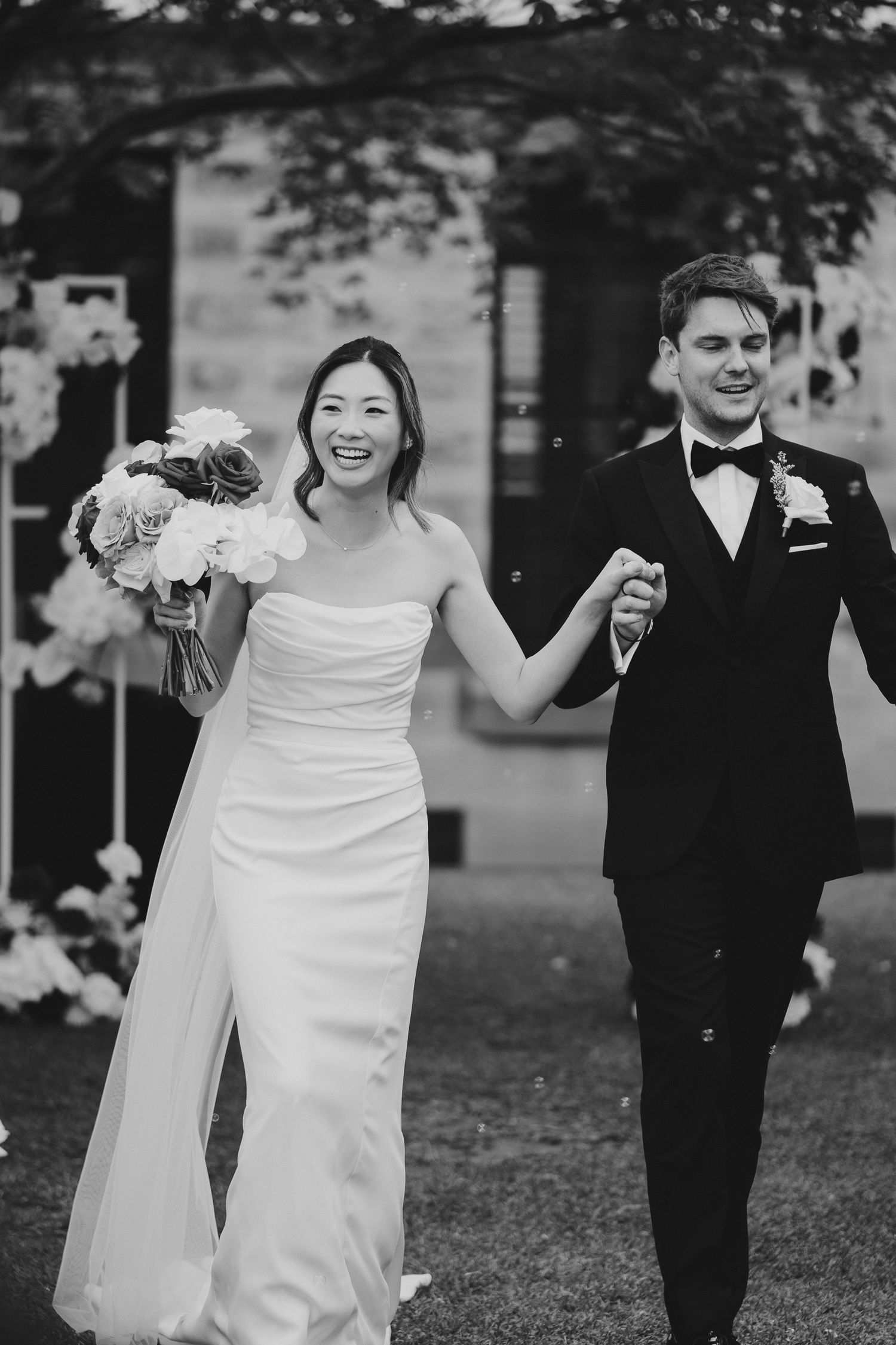 Black and white photo captures newlyweds' excited walk after outdoor wedding ceremony.
