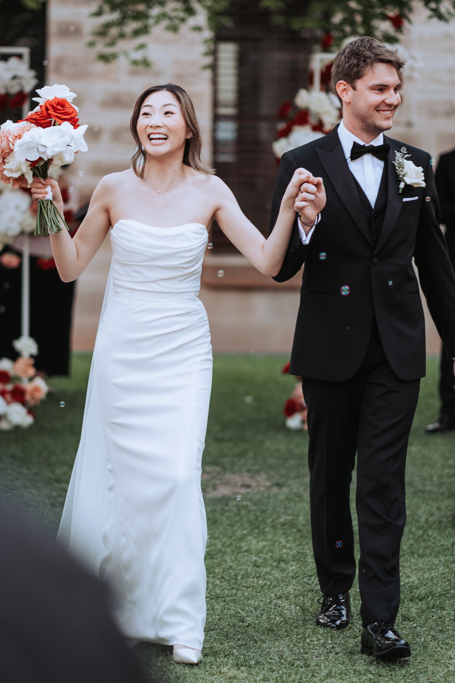 Couple celebrates their marriage walking past decorative red and white floral arrangements.