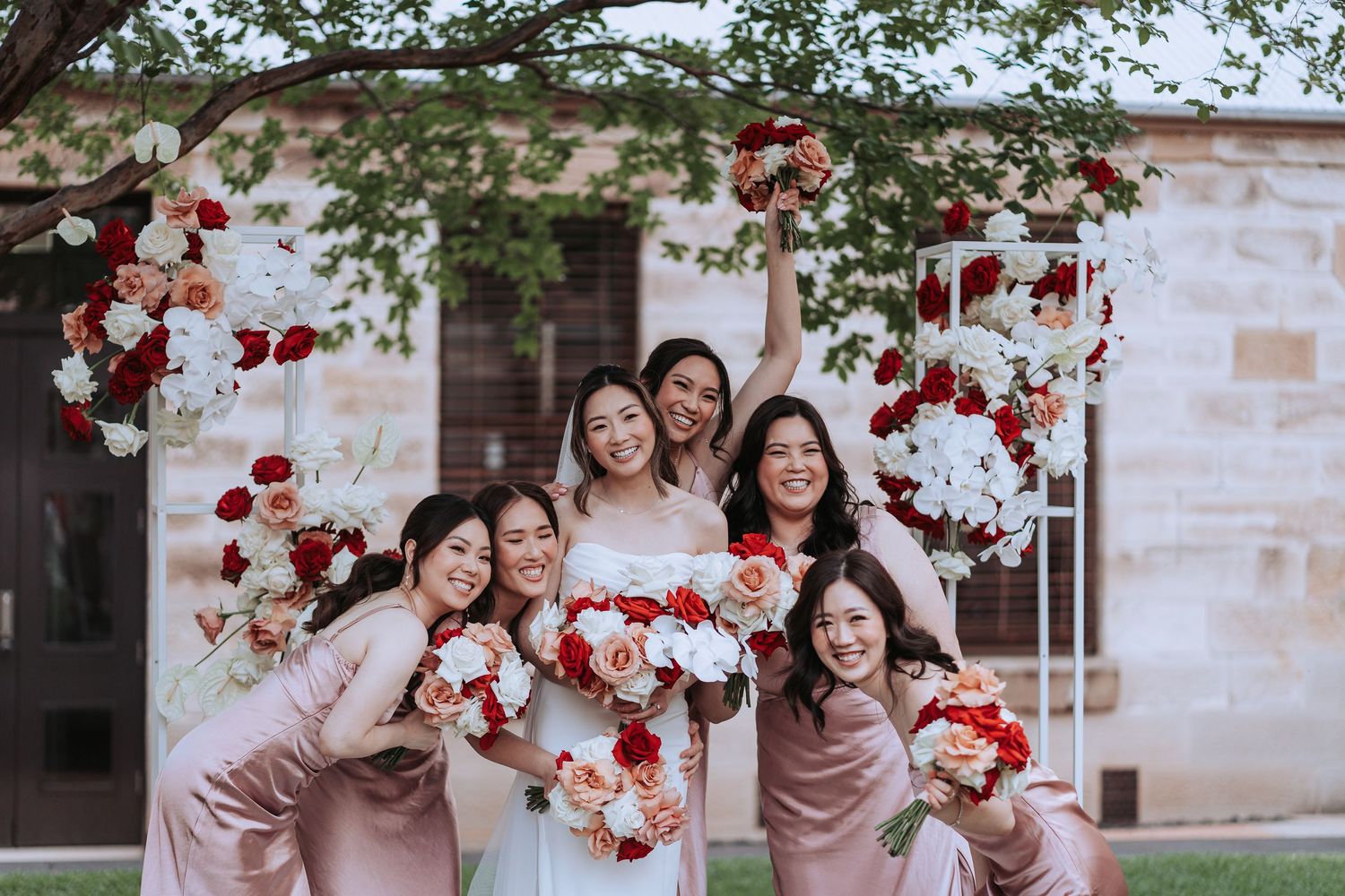 Wedding party having fun and posing with red and white floral arrangements.