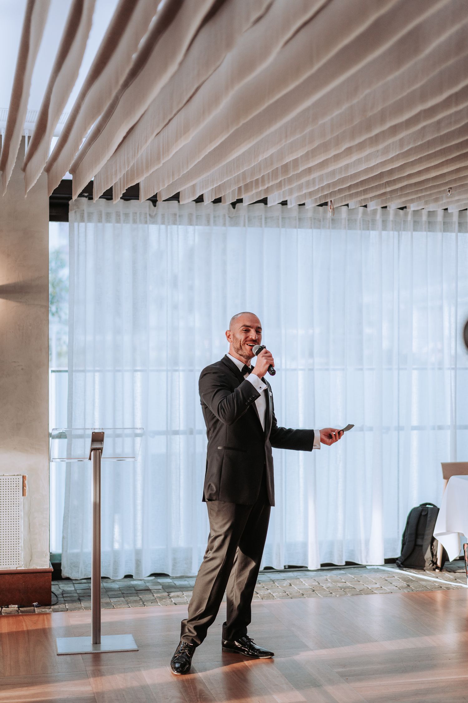 Speaker presenting in modern venue with white curtain backdrop.