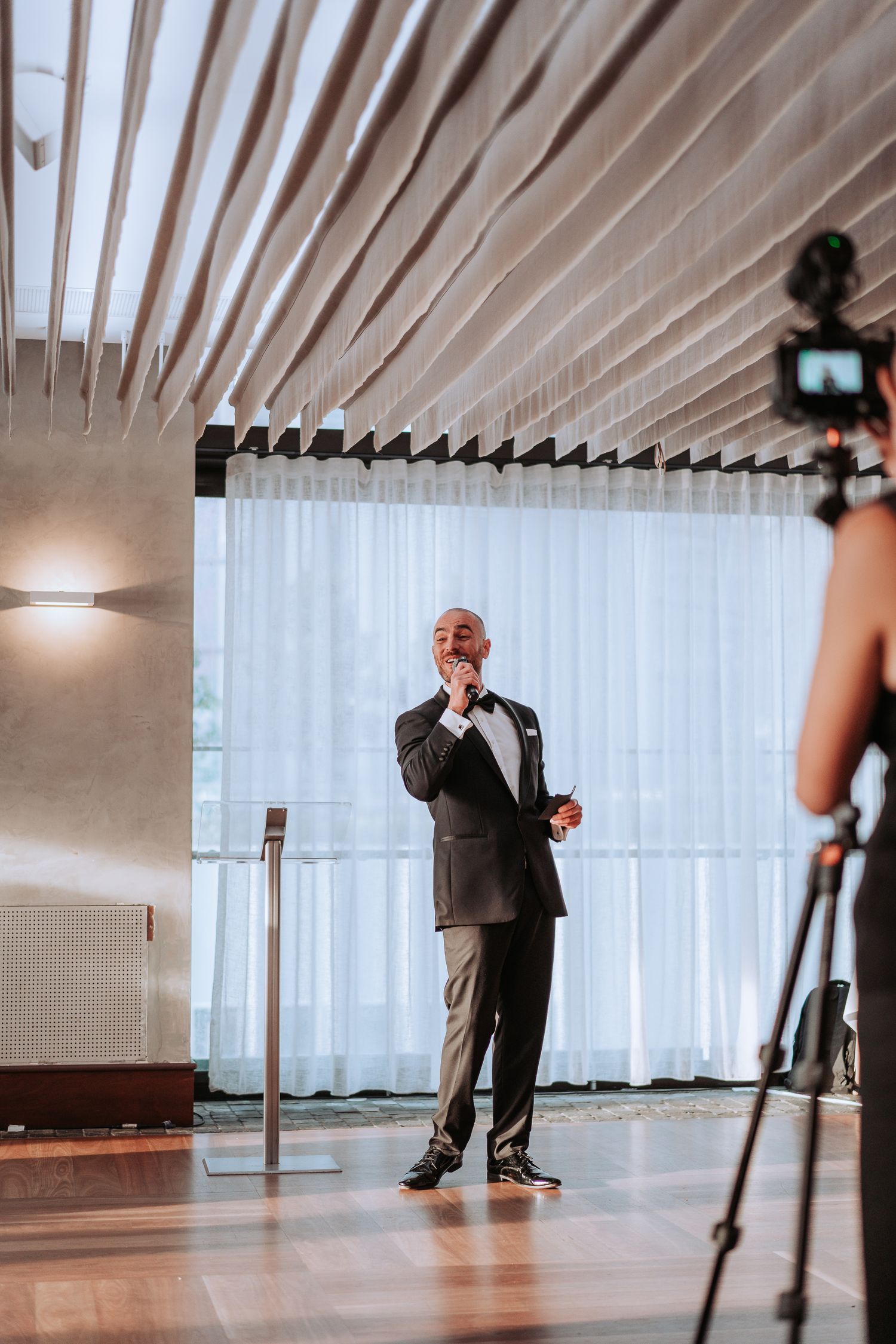 Speaker being filmed during presentation in modern venue setting.