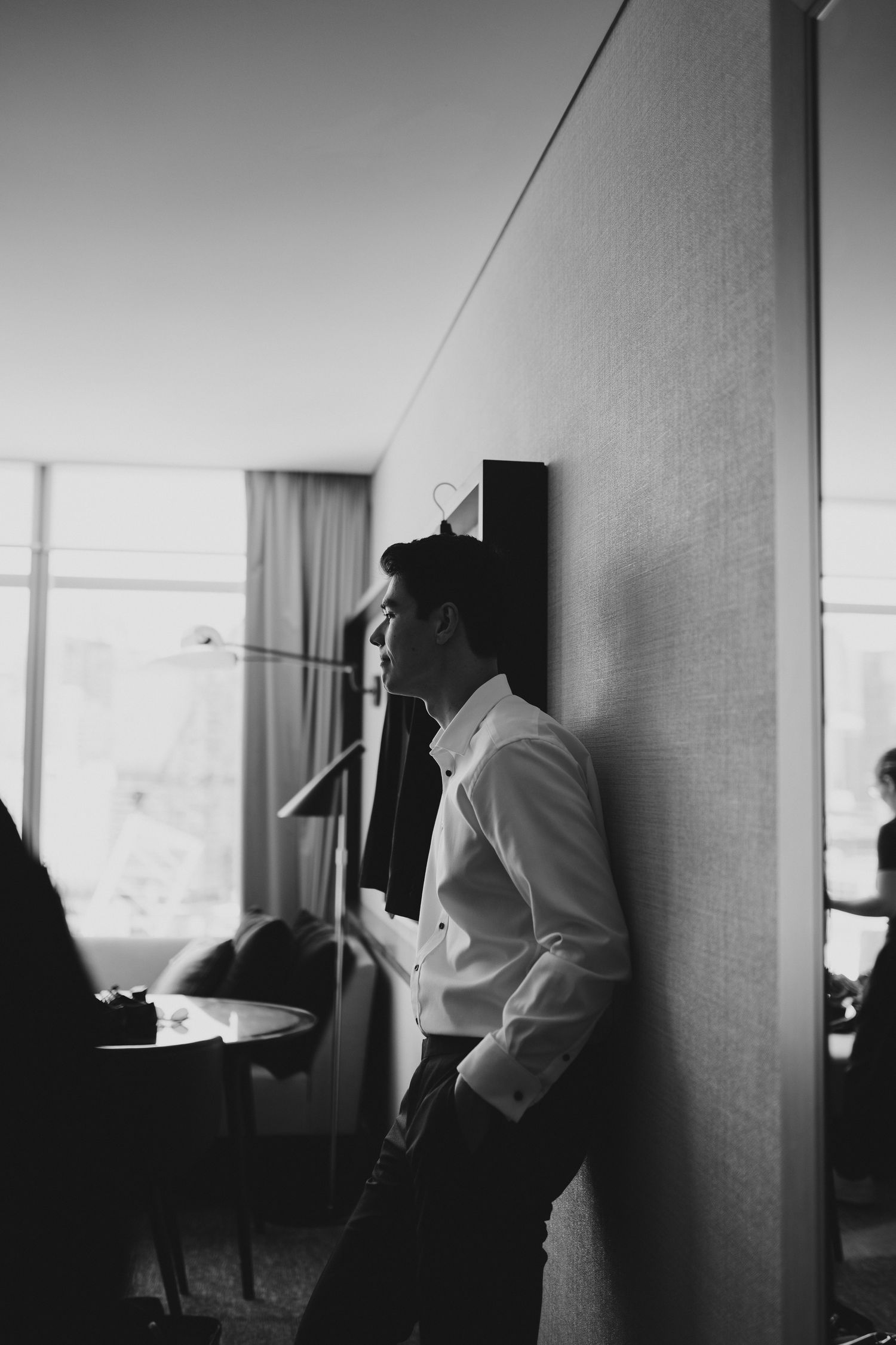 Black and white photo of someone leaning against a wall in formal attire.