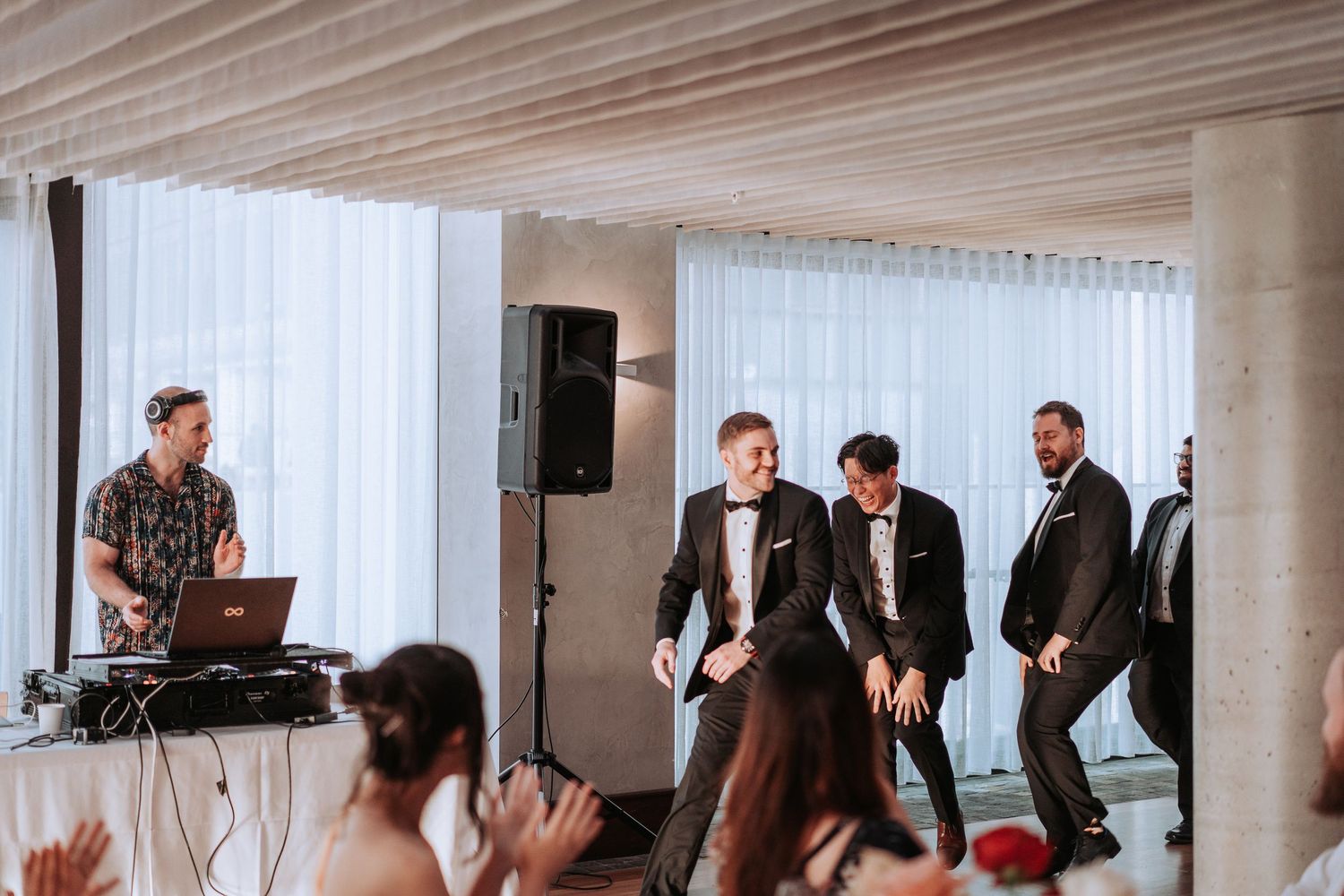 Wedding celebration with DJ and dancing guests in modern venue with white drapes.