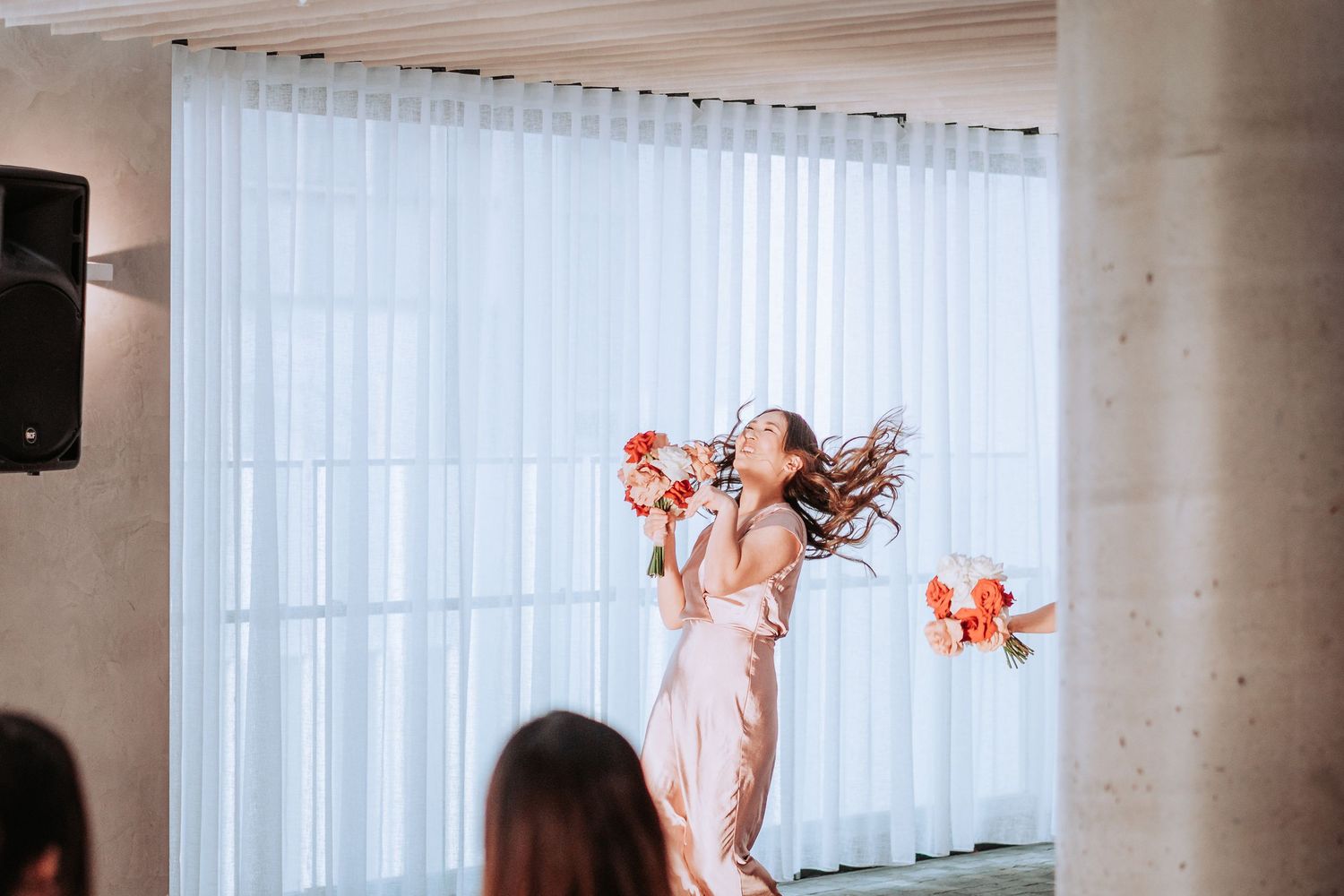 Person in pink dress dances joyfully with flowers at wedding reception.