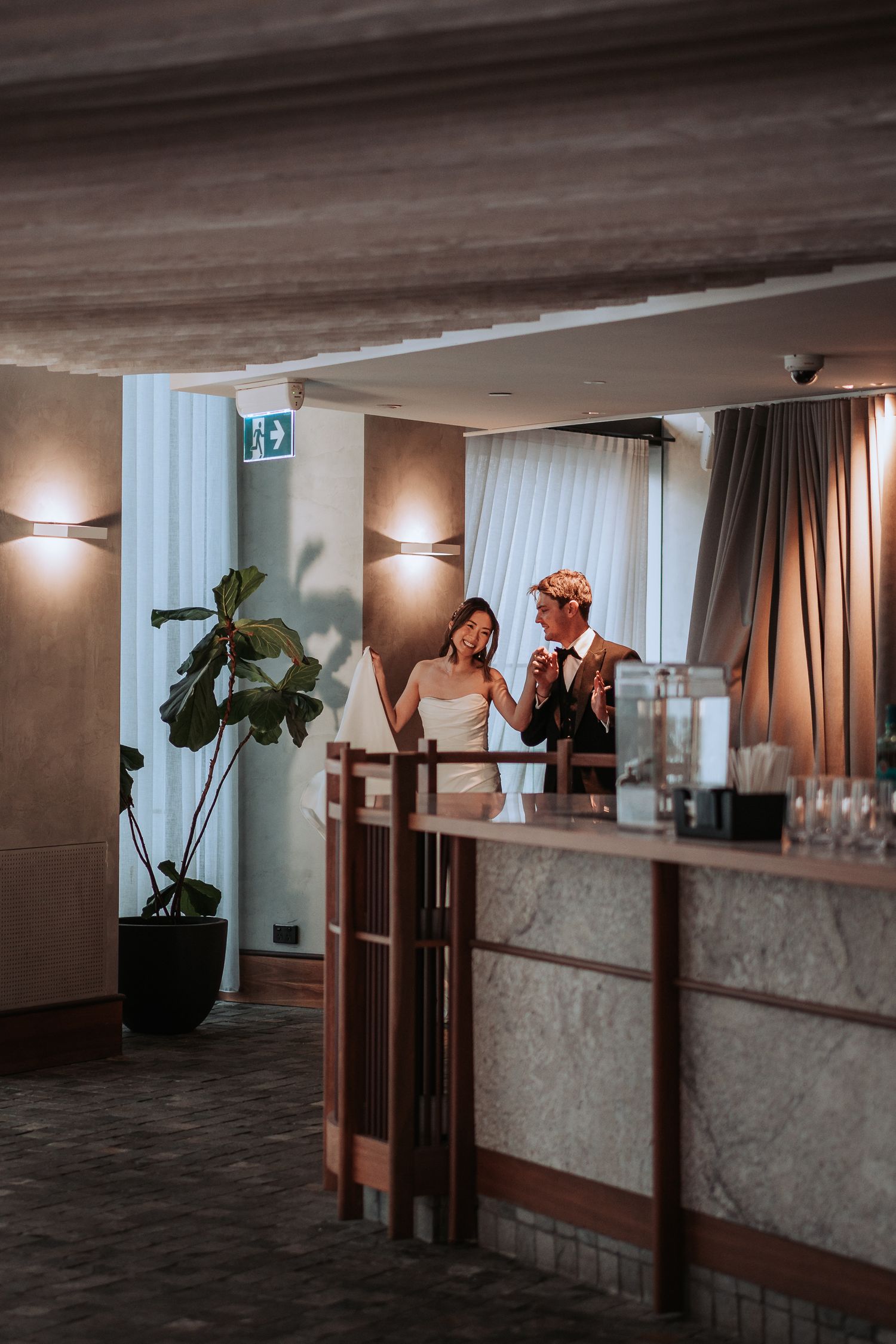 Couple shares moment at elegant wedding reception bar with modern lighting.